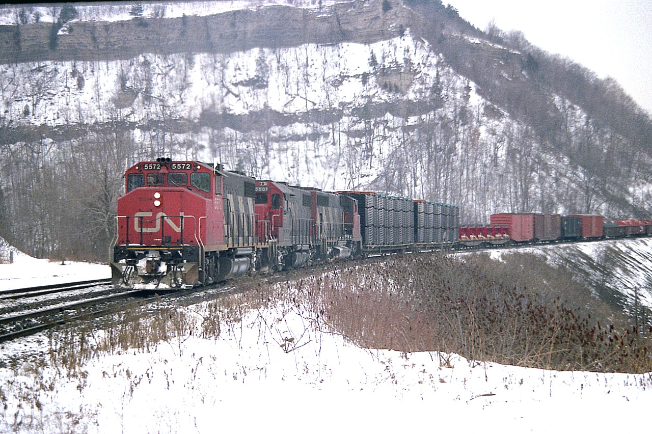 GMDs west.  CN 5572, 5507 and 9550 power a train up the grade heading westbound thru Dundas.  A typical dreary looking January day. Rather damp probably. It looks it.
This angle has long been obscured by increasing foliage over the years. A shame, but the fans have milked the angle for what it was worth. It has been 40 years since this scene, and surprisingly, the '38s still toil, now as 4772, and 4707; whereas the trailing unit was retired in 2000.