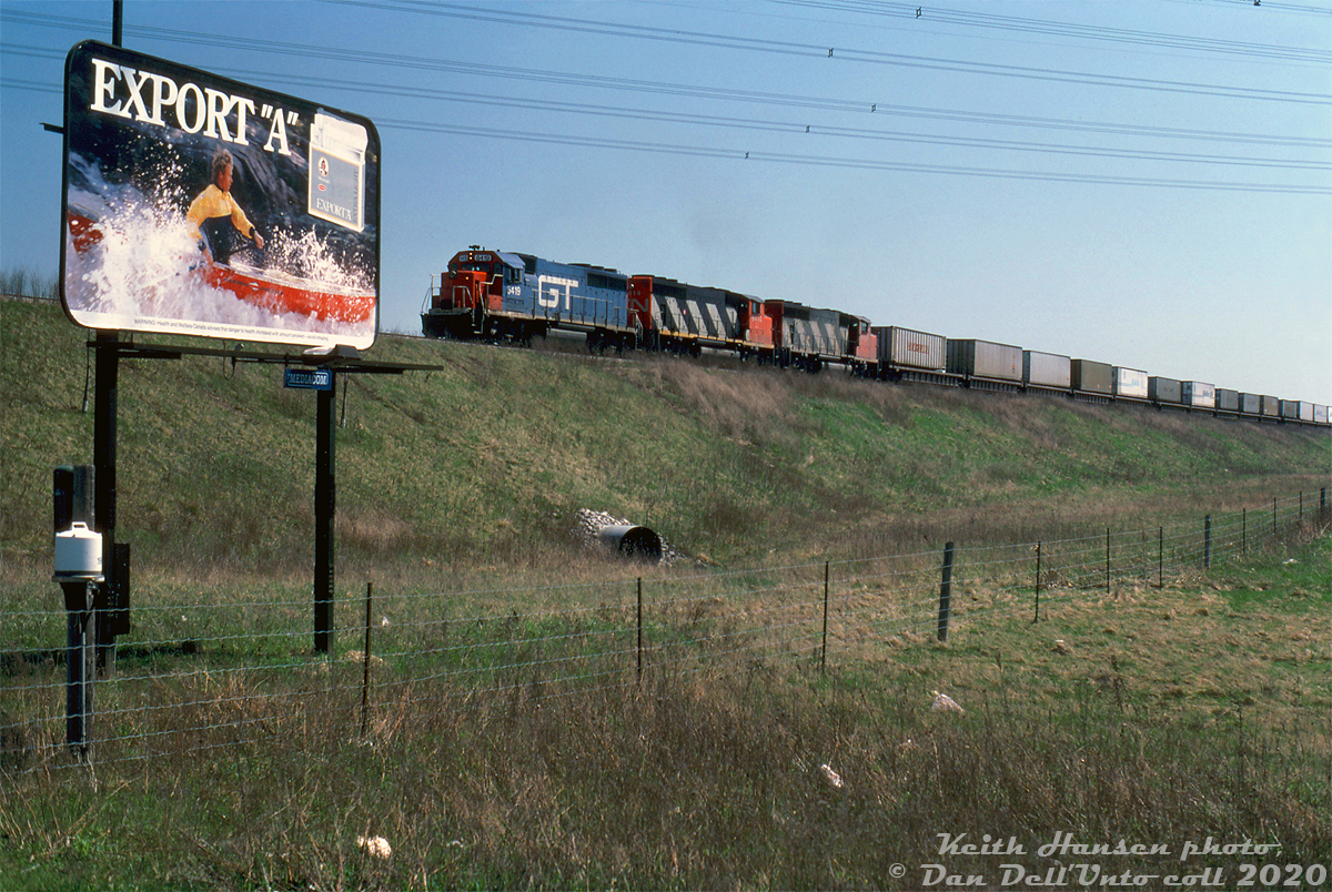 Grand Trunk Western GP40 6419 leads CN GP40-2L(W) units 9414 and a sister on a "Laser" intermodal train (likely an eastbound from the US), heading inbound to Brampton Intermodal Terminal via the leads at the south end of the yard off the Halton Subdivision, nearing the underpass at Steeles Avenue East. The large Export A cigarette advertisement hearkens back to an era not too long ago when it was still legal to publicly advertise tobacco products in Canada (that all started to vanish in 1989 with the passing of the federal Tobacco Products Control Act (TPCA)).Opened a few years earlier in 1979 on what was then Bramalea/Chinguacousy Township farmland, the Brampton Intermodal Terminal was established as CN's main intermodal hub for the Toronto/GTA area (it replaced a smaller container-handling operation inside CN's MacMillan Yard known as Conport, that opened in 1969).Another Keith Hansen photo, taken at the south end of BIT at Goreway: http://www.railpictures.ca/?attachment_id=40053Keith Hansen photo, Dan Dell'Unto collection slide.