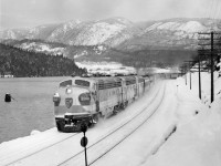 CPR's train no. 7, the first one into Vancouver powered by 4500 H.P. diesel electric on loan to the CPR from General Motors.  The train was almost three hours late.  Consisted of 13 cars and arrived in Vancouver on Friday the 13'th of January, 1950.  Burrard Inlet west of Port Moody by 1.5 miles."TEST RUN DOWN FRASER VALLEY   CPR diesel Opens New Rail Era"   By A. J. Darrymple   Out of this world!  That's the three-unit royal blue, silver and gold General Motors diesel that pulled CPR's crack transcontinental "Dominion" into Vancouver at 10:50 a.m. today in a history-making test run heralding a new era in transportation developement in Canada.  Imagine yourself at the head of a power plant 154 feet eight inches in length, with total weight of 718,000 pounds, lifting a string of 13 steel coaches, 1190 tons, up the grades and rolling around the heavy curvatures at 55 miles an hour, and you realize the thrill of railroading.  Although these diesels have been undergoing exhaustive tests in Ontario, this test run really started from Winnipeg for the 1473 miles to Vancouver under sever winter conditions.  Reporters, radio newscasters and photographers boarded the train at North Bend before dawn today for the run over the last lap into Vancouver.  A blizzard roared down the Fraser canyon; and officials of General Electric and CPR checked the operation of the three units under sub-zero conditions.  In the big, clean, roomy, clear-vision cab, the experts scanned the operational devices and speedmeter as the powerful engines sang their song of high efficiency.  Veteran Engineer Alfred Fahey handled the throttle with Fireman M. J. Marshall on the left-hand side.  While the window-wipers beat metronome time to the humming wheels, the crew, flanked by a battery of maintenence men and operating instructors, leaned forward peering through the snowy mists.  Down through Yale and then the frosty Fraser Valley, rolling toward Deroche, passing the stations in a swirl of snow, all intent upon the flashing signals.  A pin point of green.  "Clear board," sang the engineer.  "Clear board," corroborated his mate.  On through Dewdney and Hatzic, passing the eastbound Huntingdon mixed train at 9:37, and then reaching out for the curving course around Burrard inlet, and through the yards and waving crowds at the station.  "A fine trip," said D. M. Campbell, General Motors application engineer, "but we would have preferred the test under more rigorous conditions; 15 below was the worst we went through."  Regardless of the weather, CPR chalked up another first; the first of such power units to be used in transcontinental passenger train through the Rockies; recalling another first, that day, May 23, 1887, when old No. 374 pulled the first passenger train into Vancouver.  Now the trend is distinctly from time - honored steam to diesel; lower fuel, maintenance and labor costs; improved schedules through reduction of service steops.  Example:  Winnipeg - Vancouver run steam locomotives make 32 stops for water; diesels 10.  For the passenger:  Smoother stops and starting and a more restful ride; and for the romantic - minded rail-fan, a sleek machine in brilliant color designs, running swiftly and purring like an electric clock.  CPR officials aboard were T. F. Donald, Winnipeg, assistant superintendent of motive power; G. H. Nowell, Vancouver district master mechanic;  Al Cowburn, assistant superintendent, North Bend; W. Sinclair, Montreal, diesel equipment engineer;  B. W. Woodland, Winnipeg, internal combustion equipment superinvisor; Ernest Hanson, Vancouver, diesel supervisor for Pacific region.  General Motors officials:  H. D. Dana, assistant general servicee manager;  R. E. Hunter, sales director;  Don Campbell, engineer;  Mel Johnson, service and maintenance engineer;  Frank Switzer, Ed Park, E. Formento, operating instructors.