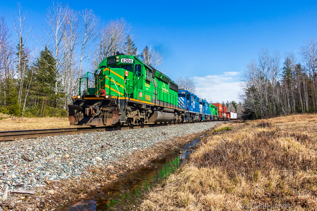 A green and blue consist charge NBSR train 907 as they head through Vespra, New Brunswick.