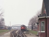 These were the lean years for Amtrak. This train which rattled its way along the CASO from Detroit thru to the International Bridge to Buffalo was given the name "Niagara Rainbow" a rather inventive name for such a clunker.
This train during these lean years ran with old hand-me-down E8A units, as seen in this image. AMTK 407 is photographed on approach to the bridge having just stopped at the passenger station. A few people and a taxi can be seen. On the right in this image is the old B-1 station, moved in 1981 to Oakes Park down on Central Av to keep the old CNR 6218 company. A lot of things have changed in Fort Erie over the years...on the left, the water tower is gone, as is the crew hostel in front. The bridge recently was replaced. In far background the CN shop has been closed and is now a fledgling RR museum. And the Sidekick of the day was along; standing in front of the pole on the left. 