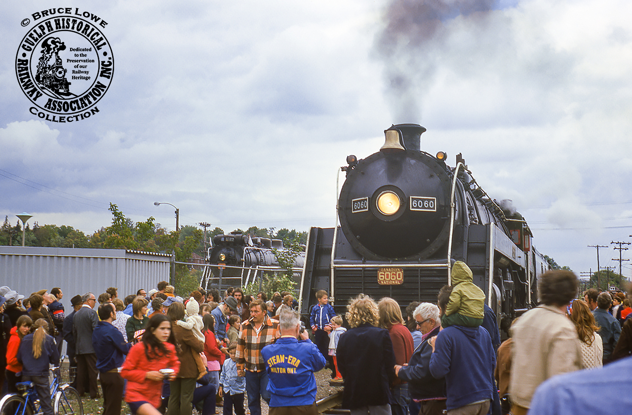 The people are everywhere at Guelph station on September 21, 1975 which saw CNR U-1-f “Bullet Nosed Betty” 6060 leading an excursion chartered by the Buffalo Chapter of the National Railway Historical Society from Niagara Falls to Guelph via Lynden on the Fergus Sub.  The 4-8-2 Mountain type locomotive, built in 1944 by the Montreal Locomotive Works, is seen posed alongside CNR 4-8-4 Confederation type 6167, which was retired from these same excursion duties 11 years prior.  Today CNR 6167 can still be found in downtown Guelph, recently relocated to its third home in Priory Park.  CNR 6060 is now under restoration by the Rocky Mountain Rail Society in Stettler, Alberta.More from this day:Nortbound at Harrisburg by Bryce Lee.Photo runby near Guelph by Bruce Lowe.At CN Guelph Junction by Bill Thomson.