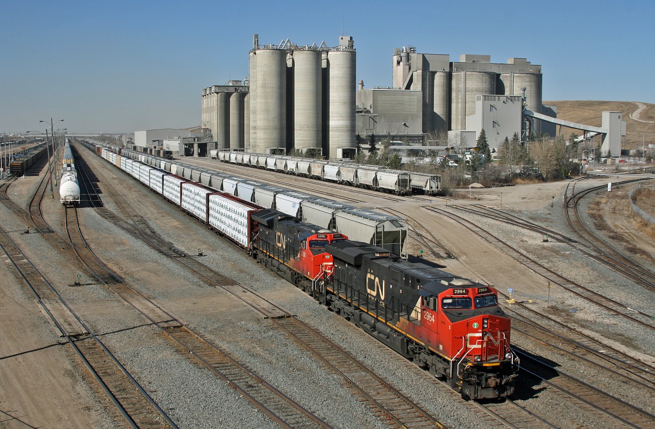 CN A 41251 13 rolls past Bissell Yard and the looming Leigh Cement plant in Edmonton, Alberta.  CN 2964, CN 3090 and mid train remote CN 2971 make easy work of this 178 car train.