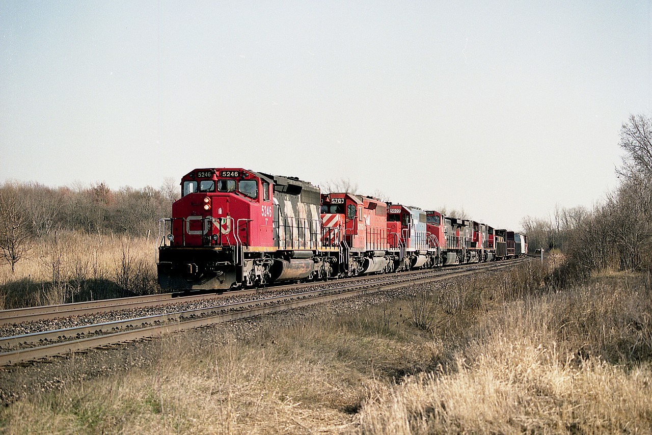 Back when I quit work, late winter 2005; one of the things I vowed to do was wean off work slowly. The very idea of getting up every day at 0345 to report an hour later was a constant thing; and to all of a sudden doing nothing would not be good for my health. The shock to the system has led to an early demise for some; and I was not going to let that happen to me......so......the first couple of months into retirement; I still got up early and went out the door, only now to the tracks. Gradually I got up later and later and stayed out less. I'd hate to be going that route now, seeing how few trains there are.
Having said all this; I've presented my excuse for hanging around Tansley. I was there most every morning. It was the sun angle. Not bad at all in the morning.
In this shot; I checked my log and I must have been there most of the day, for the sun angle here looks to be around 1400 hrs or so as this train is running roughly northbound at this point on its way to Mac.  I am at No. 1 Side Road, a dead end off Tremaine Rd. Nice place to park and listen the scanner and read the paper. I parked on the north side of the road, actually Milton; and the south side is Burlington. Approaching the crossing is a nice combination.......CN 5246, NREX 5703 (x-CP), GT 5922, and CNs 2677, 2547, 5781.
Not much scenery, but a decent train.