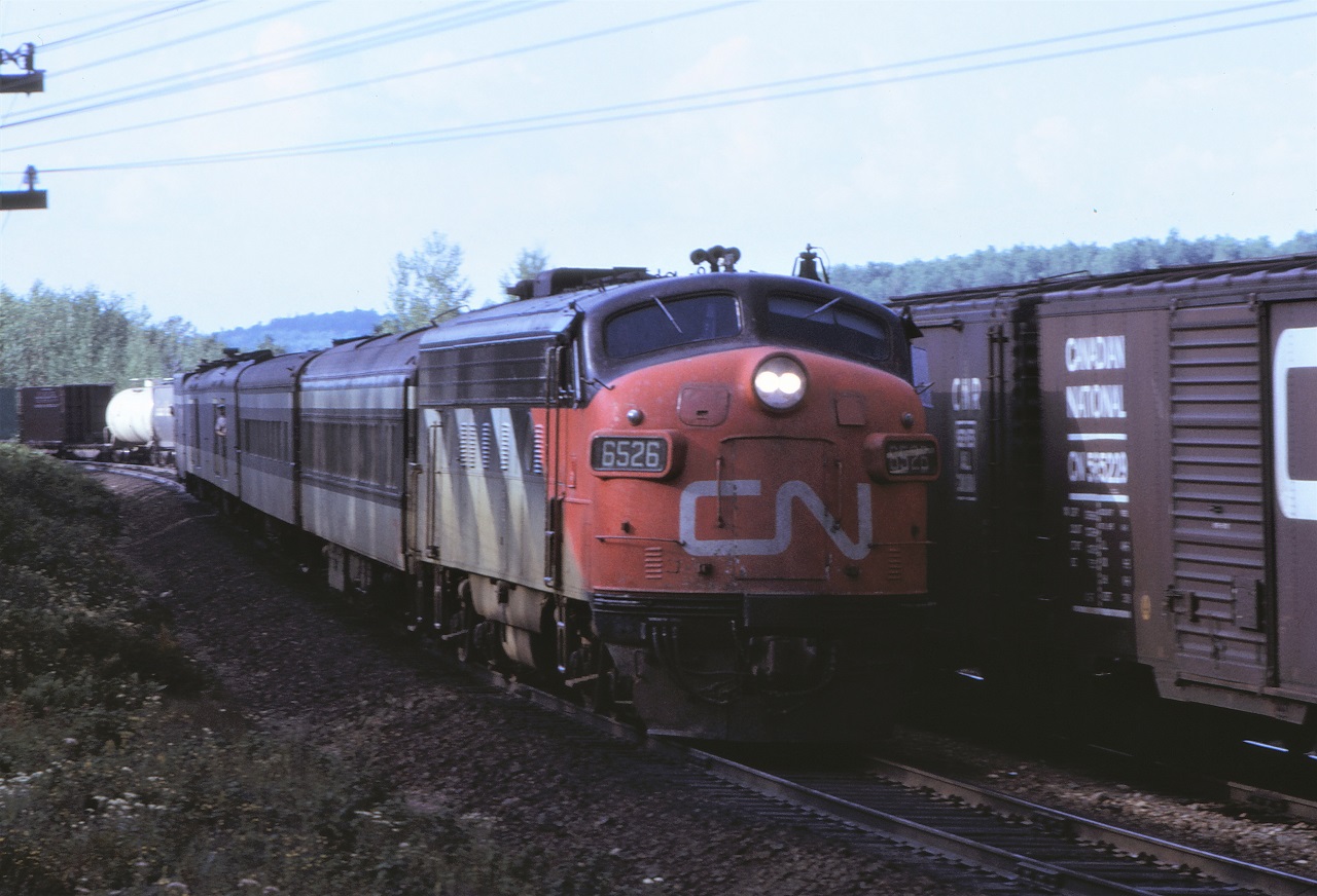 CN's Nakina to Capreol passenger train number 676, slows for its station stop at Laforest, Ontario as a westbound freight pulls through the passing track.  Power for the four car train is FP9A 6526 with steam generator car 15450 bringing up the rear.
