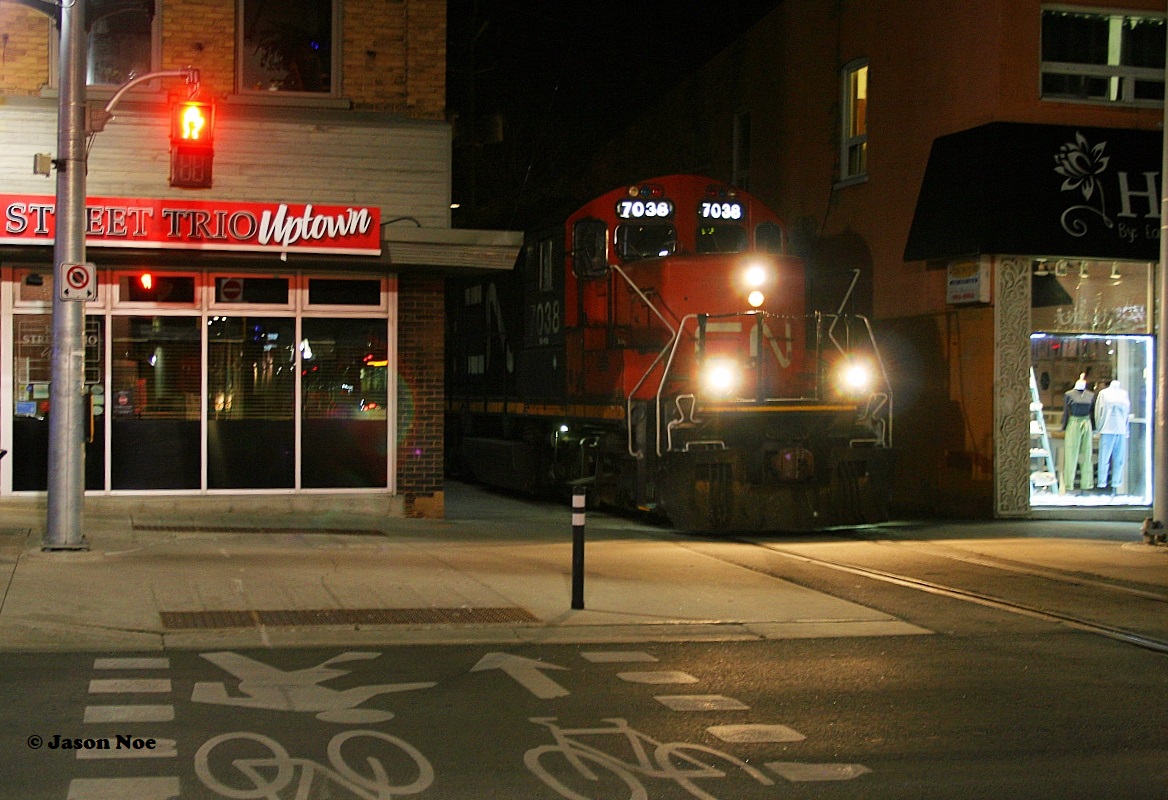 CN GP9RM 7038 solely leads L566 through Uptown Waterloo approaching King Street just before midnight as it heads to Elmira on the Waterloo Spur.