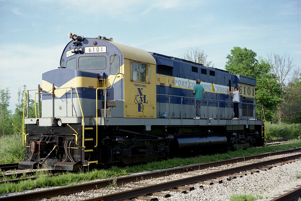 New country.  New name.
It is as easy as this. Just like an 'iron on' patch, the new name Port Colborne Harbour Railway is applied to what was very recently the New York & Lake Erie C-425 from over the river.  Yeah, it looks easy, but these two guys seemed to have a real problem getting this lettering on straight.  This was late in the day. Maybe the voracious mosquitos were bothering them. I know they sure tested me.  The official Grand Opening of the new PCHR (now GIO Trillium) was less than 10 days away.
The locomotive worked the PCHR as their only unit at the start up; and went back to the NYLE in 2001. In 2007 it was dealt to the Delaware-Lackawanna at Scranton, PA, where it still rolls today. It began in 1966 as PRR 2423, so it has had a good life.
