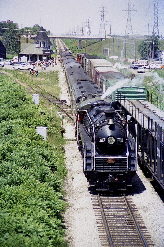 This image is similar to one I posted about 6 years ago; but is more favourable in CN 6060 being much closer to the camera as I stood looking west on the Maple Av overpass in Grimsby. I am very grateful for the shots taken here, as this was far in advance to any thought of relocating to Grimsby myself, which I did 24 years later. Any shots of the beautiful station I am appreciative of, as it burned down last day of 1994.
Crowds used to come out to greet ol' Bullet Nosed Betty, as this oil fired locomotive was nick-named; and it was sad to see the demise of the twice a week summer runs from Toronto to Niagara and return. The loco developed boiler problems, I think it was, and there was not the money for overhaul. Thankfully, Alberta had a more positive view of the value of this classic, and so the engine went West.