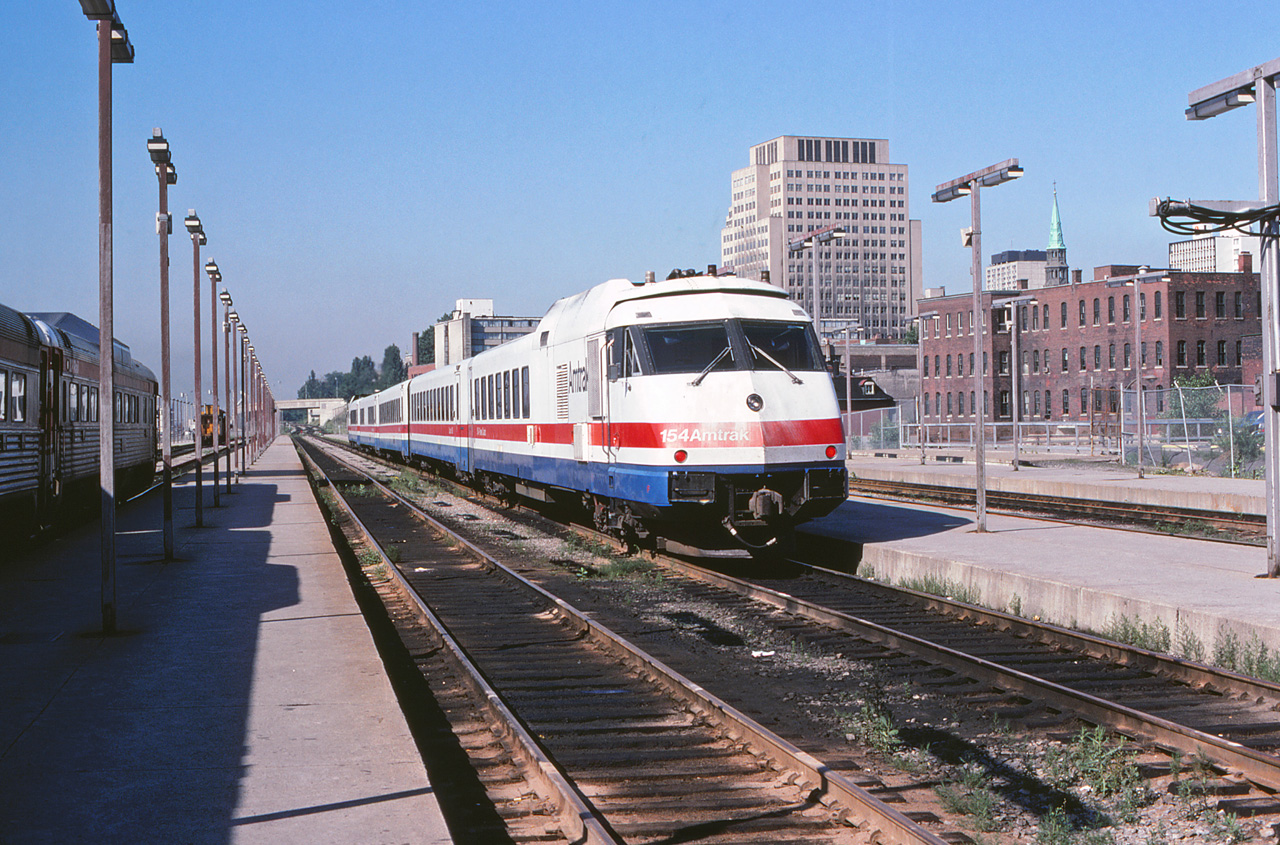 In 1980, the Amtrak "Adirondack" still operated into CP's Windsor Station in Montreal, while the overnight "Montrealer" used CN's Central Station. The D&H PAs and conventional equipment have given way to a Rohr Turboliner. Here, power car 154 is trailing as the train departs for New York City.The RDCs at left are likely in West Island commuter service, although at this time VIA still operated RDCs to both Ottawa and Quebec City over CP's north shore lines (via Lachute and Trois-Rivières respectively), and much of that equipment would have still been in CP colours.