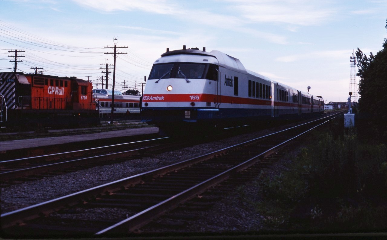 After early success with its French-built Turboliners, Amtrak ordered seven train sets based on the French design (but built by Rohr in California who had obtained a license from ANF. These trains used carbodies, wheels and engines brought from France while Rohr was responsible for the cabs and interiors. The trains were delivered in the second half of 1976 and assigned to "Empire State Service" in New York state, including runs to Montreal. In this photo we see nearly new car 159 leading the Adirondack past CP's Glen coach yard on the final lap of its trip from Grand Central station in New York to Windsor Station in Montreal. These train sets continued to serve Amtrak until the mid-1990s. The 159 was part of a group of cars removed from service for rebuilding in 1994 as the prototype for an "RTL II" modernization program. Alas, that was the only train set completed and it ran until 2002. (With supplemental information from Dale Johnson's book "Trail of the Turbo, The Amtrak Turboliner Story".)