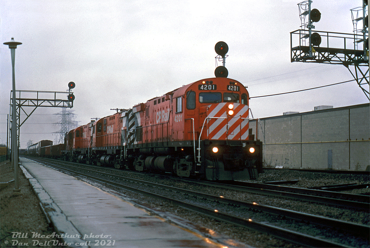 April showers bring May flowers: with white lights lit up on the lead unit, four CP 4-axle MLW's head eastbound on CN's Oakville Sub through Burlington West on an extra freight, exercising trackage rights from Hamilton Junction to CP's Canpa Sub at Canpa (near Mimico). CP C424 units 4201, 4225, another 42xx sister and an 87xx RS18 lead the consist.

A little-known tidbit is 4201, the first conventional CP C424 built (4200 was a unique earlier phase one-off) sports nose-mounted flag brackets, one of only two units delivered with this feature (4200 was the other). Units 4200-4209 also originally had high-mounted headlights on the flat part of the cab that were relocated to the nose in the late 60's, matching all the other C424's in the fleet. Trailing 4225 sports the "flipped intake grills", apparently installed incorrectly during painting and subsequently flipped to the correct orientation here (many units ran around like this until the grill paint was properly touched up). By this time, the C424's had all been upgraded for roadswitcher service with extra rear pilots, headlights and numberboards, but there were still unrebuilt 8700's like the trailing unit around.

Bill McArthur photo, Dan Dell'Unto collection slide.
