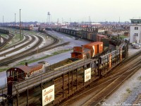 It's a busy summer evening at Toronto (Agincourt) Yard, as viewed from the Finch Avenue overpass at the north end of the yard. A cut of empty open autoracks are being moved around in the foreground as CP S2 7026 switches a mix of cars on the next track over, including a gondola full of freight car wheels in front of its caboose (maybe to/from the car shops). CP 7026 wasn't one of the regular pulldown power units that flat-switched the east end of the hump yard (those were usually a pair of MU'ed MLW S2 or S3 switchers, and only certain numbers were so equipped like 7077+7089, 6563+6564, etc) so 7026 might be working a local, transfer or road job that's just dropping in.
<br><br>
Road freight power in the form of modern MLW and GMD units are visible in the background, with one set running light power (likely heading from the diesel shop in the distance to their train in the yard).
<br><br>
Much of the freight cars in this scene are still in CP's block lettering or script lettering liveries, as new and repainted Action Red cars were just starting to show up. Three vans (in the late 60's <a href=http://www.railpictures.ca/?attachment_id=33301><b>"Action Script"</b></a> colours) are visible on the left near the van shop. On the right is the East Yard Pulldown Tower. Goodies visible in the yard include stock cars (sprayed with white disinfectant lime), covered gondolas, and an old combine passenger car (possibly removed from its trucks and used for storage).
<br><br>
<i>Keith Hansen photo, Dan Dell'Unto collection slide.</i>
<br><br>
More of Toronto-assigned CP S2 7026 around town:
<br>
Working the "Old Bruce" service track in West Toronto: <a href=http://www.railpictures.ca/?attachment_id=38483><b>http://www.railpictures.ca/?attachment_id=38483</b></a>
<br>
Crossing Strachan Avenue at Parkdale Yard: <a href=http://www.railpictures.ca/?attachment_id=35550><b>http://www.railpictures.ca/?attachment_id=35550</b></a>