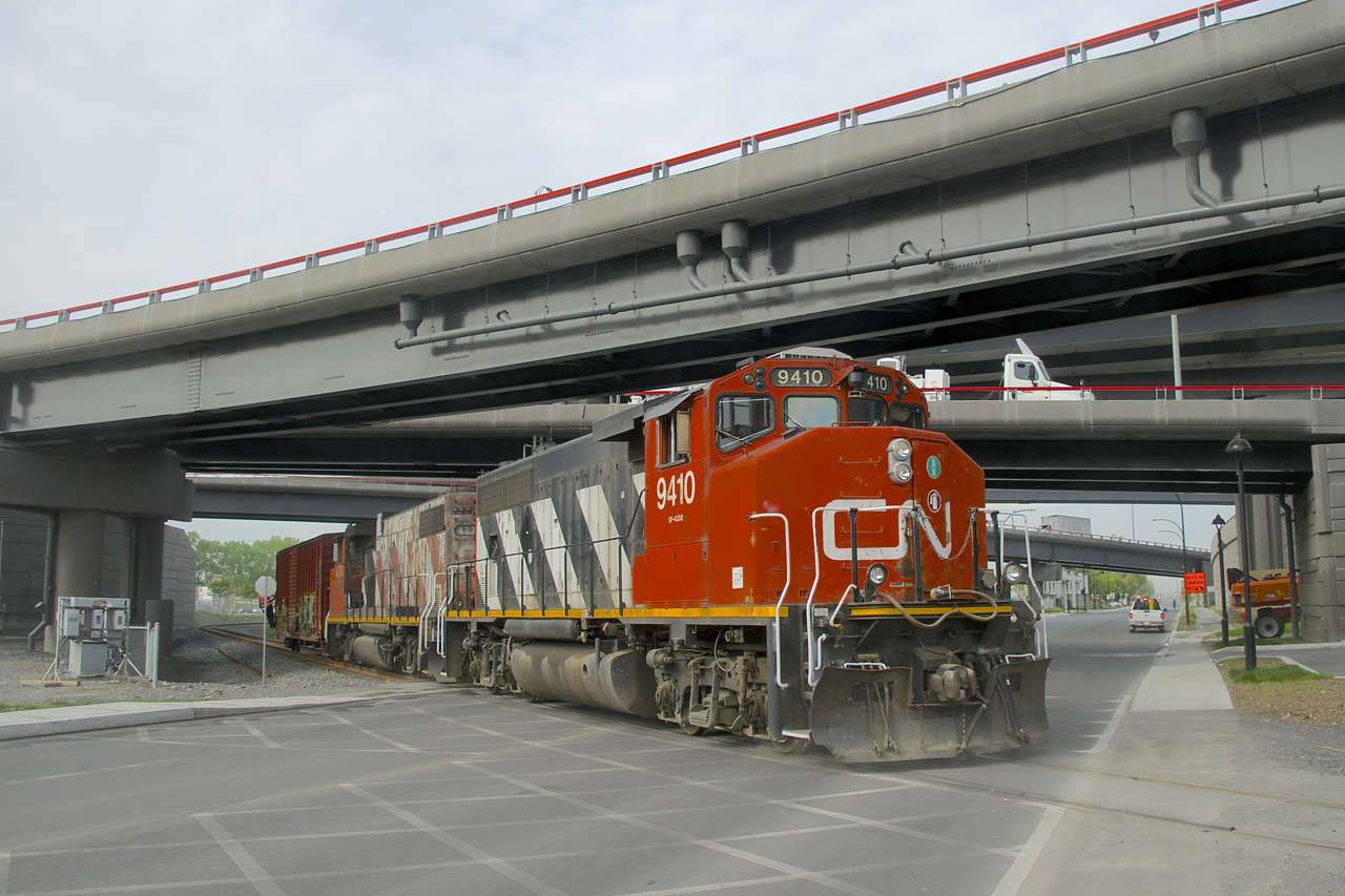 The Pointe St-Charles Switcher is shoving a single boxcar towards the Kruger plant as it passes over the Notre-Dame Street crossing and underneath the recently rebuilt Turcot interchange. Power is very clean CN 9410 and very faded CN 4774.
