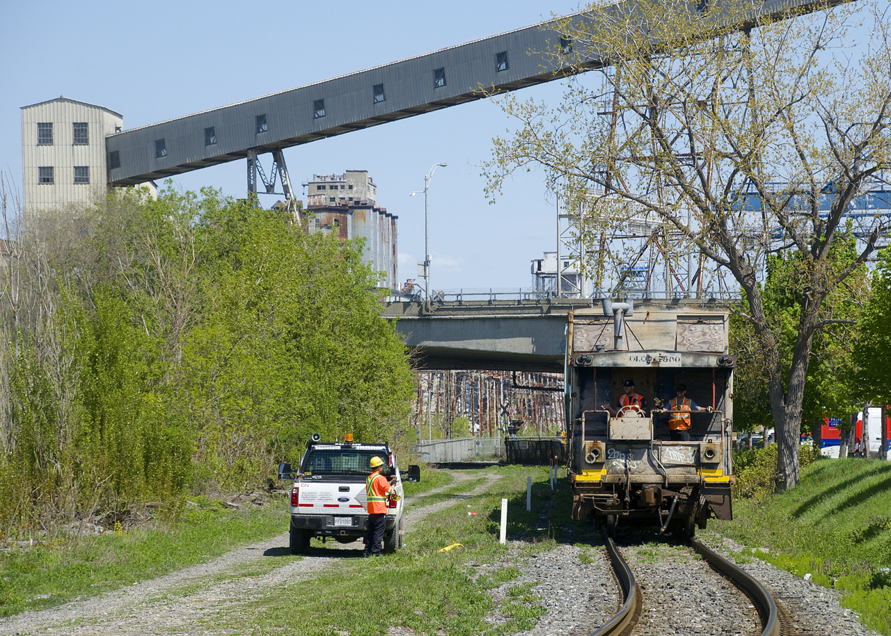 The Pointe St-Charles switcher is returning from switching a couple of clients, with a shoving platform leading back to the yard. A couple of crewmembers wave at a foreman who had just removed a red flag and derail on this section of track.