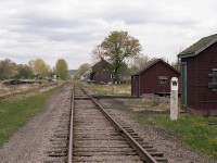 Just a photo looking along the CN line, eastward. This is offered as an example of how it "used to be". Going into the village were storage buildings, equipment buildings, track car sheds and many other nondescript structures, as shown here. Most communities had stub tracks (or old team track)  usually with old flat cars and the like taking up space, often appearing derelict. Once the 'great demolition era' of the mid 70s got into full swing, with stations and misc buildings coming down everywhere; the railroad just became a line thru town and, not long after, branch lines abandoned and the rails pulled up.
Such is the case in Stirling.  The "save the station" committee in this community rescued the station seen in the right side background, but everything is now gone.