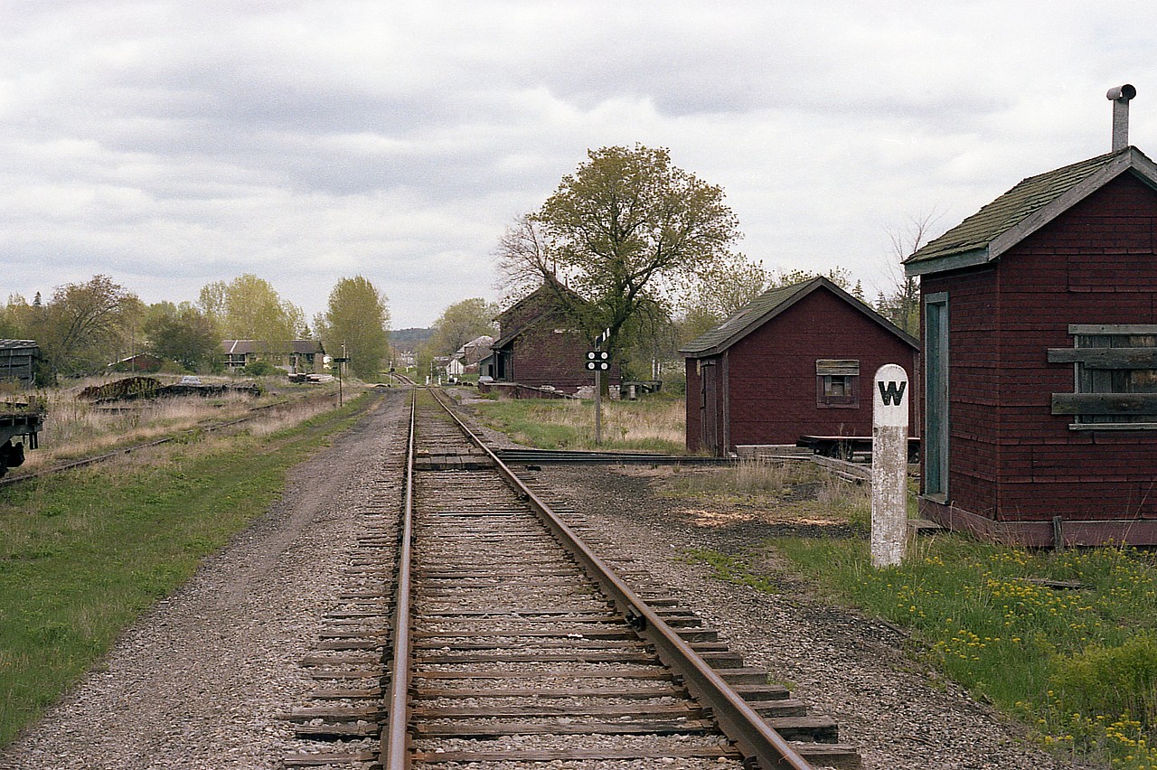 Just a photo looking along the CN line, eastward. This is offered as an example of how it "used to be". Going into the village were storage buildings, equipment buildings, track car sheds and many other nondescript structures, as shown here. Most communities had stub tracks (or old team track)  usually with old flat cars and the like taking up space, often appearing derelict. Once the 'great demolition era' of the mid 70s got into full swing, with stations and misc buildings coming down everywhere; the railroad just became a line thru town and, not long after, branch lines abandoned and the rails pulled up.
Such is the case in Stirling.  The "save the station" committee in this community rescued the station seen in the right side background, but everything is now gone.