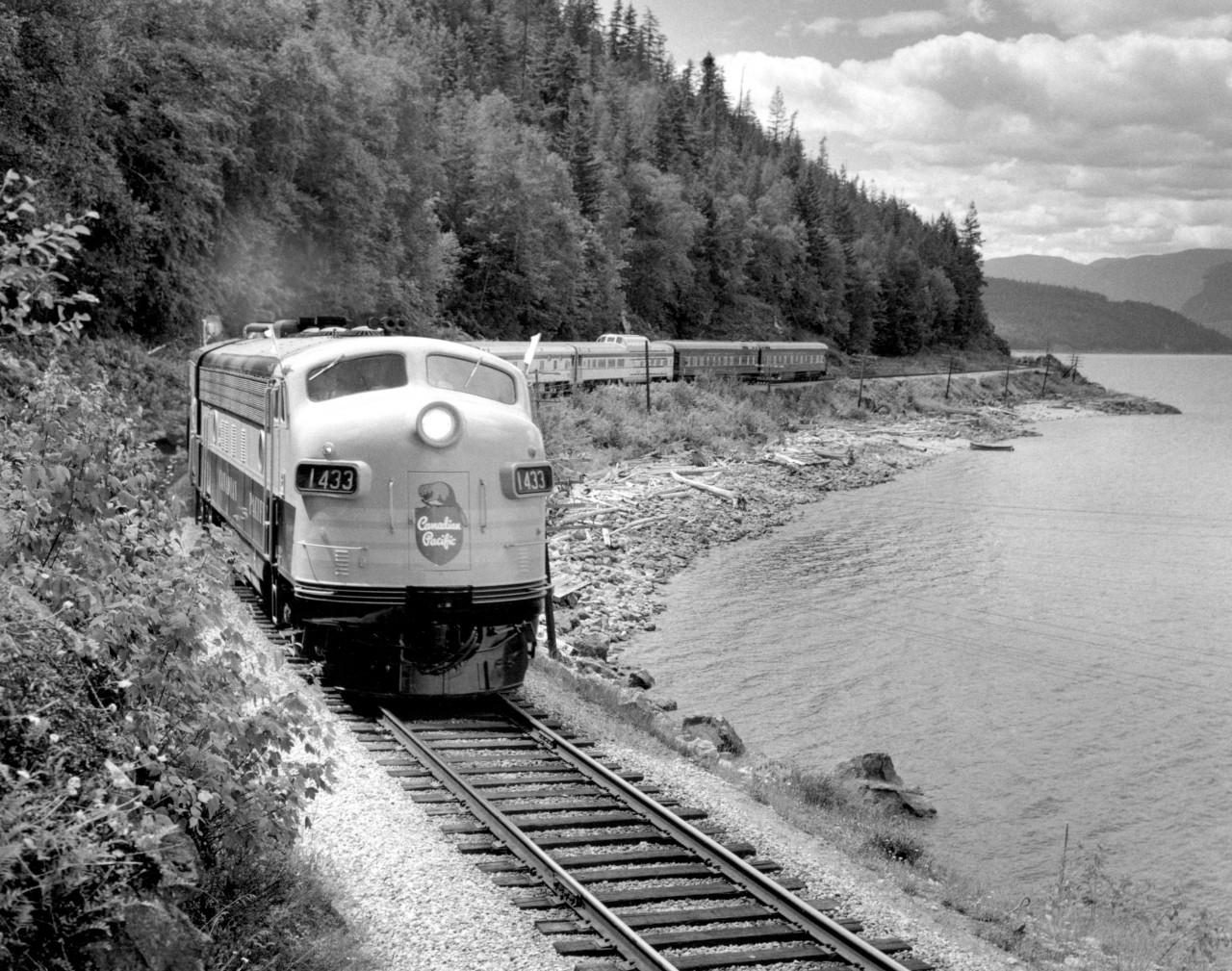 The centennial celebrations of the Province of B.C.'s becoming a Crown Colony in 1858 were marked by a visit of Princess Margaret to the Province.  Upon leaving Vancouver for Banff, the CPR provided the Princess with a 9 car special, including one dome & two business cars, which special train is seen here, July 29, 1958, on the shores of Shuswap Lake, 72 miles east of Kamloops.  Waiting behind spiked switches, all opposing passenger trains cleared X E 1433 by one hour, freight trains by 5 hours.