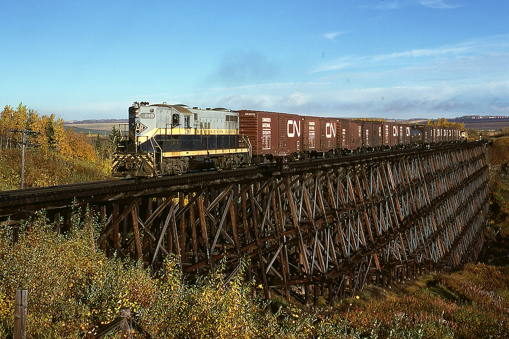 Eastward from Dawson Creek, BC, on Northern Alberta Railways, there were two large timber trestles, first at mileage 134.7 over Dawson Creek east of Iracard and second at mileage 131.5 over Bissette Creek just east of Pouce Coupé.  This is the long one over Dawson Creek and just 3.3 miles east of the town, built in 1951 to replace a challenged one a few hundred feet downstream (to the right), here carrying timetable train No. 52 (a Tuesday, Thursday, Saturday wayfreight returning to Grande Prairie, AB) on Tuesday 1977-09-20 with GP9 210 and thirteen cars plus caboose.

A similar shot, but taken three years later from an elevated viewpoint up a tree, is on the back cover of the recent NAR Diesels book by Les Kozma.