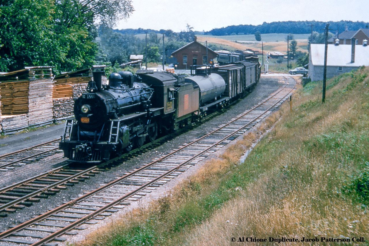 The time is 1225h as CNR daily except Sunday mixed train M329 departs Mildmay en route to Southampton with CNR 1560 getting the consist up to the 35mph track speed.  The venerable H-6-g ten wheeler stabled at Palmerston will handle various switching duties along the way, meeting counterpart M330 (Southampton - Palmerston) at or near Paisley, where both are due at 1330h.  Per the 1957 Employee Timetable, M329 would depart Palmerston at 1130h arriving Southampton at 1420h, while counterpart M330 departed Southampton at 1230h, arriving Palmerston at 1545h.  Note the wig wag signals between the main track and siding, the vintage automobile waiting for the mixed to pass, and the house at upper right in the distance.  This house, at 23 Absalom Street West would briefly become "The Station Tavern" in 1992 with a former CNR heavyweight passenger car trucked in from Harriston.  The Southampton Sub had been lifted circa 1989.  The car was scrapped after the tavern closed circa 2010.Originally part of the Wellington, Grey & Bruce Railway which was chartered to build from the Galt & Guelph/Great Western Railway at Guelph to Southampton in 1864, what would become the CNR Fergus and Southampton Subdivisions was laid between 1869 and the end of 1872, with rails reaching Mildmay in early 1872.  The station pictured is a Wellington, Grey & Bruce Railway standard Type B station - measuring 60 feet x 30 feet - built circa 1872 and would be demolished in 1971.*CNR 1560 was built by MLW in 1912 for the Canadian Northern Railway as their 1370, renumbered to Canadian National 1370 in 1919, and to CNR 1560 in November 1956.  Less than three years after this photo 1560 will meet the scrapper's torch in March 1960.*Information per Peter Bowers' Two Divisions to Bluewater.Original Photographer Unknown, Al Chione Duplicate, Jacob Patterson Collection Slide.