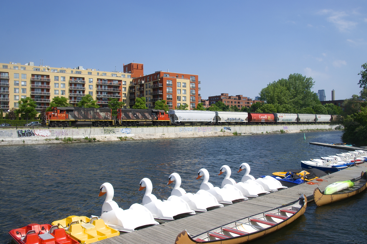 On a scorcher of a morning, the Pointe St-Charles switcher is heading to Ardent Mills with six grain loads (and a single car for O-I Canada) and CN 4706 & CN 4707 for power. On the other side of the Lachine Canal are a number of pleasure crafts available for rental.