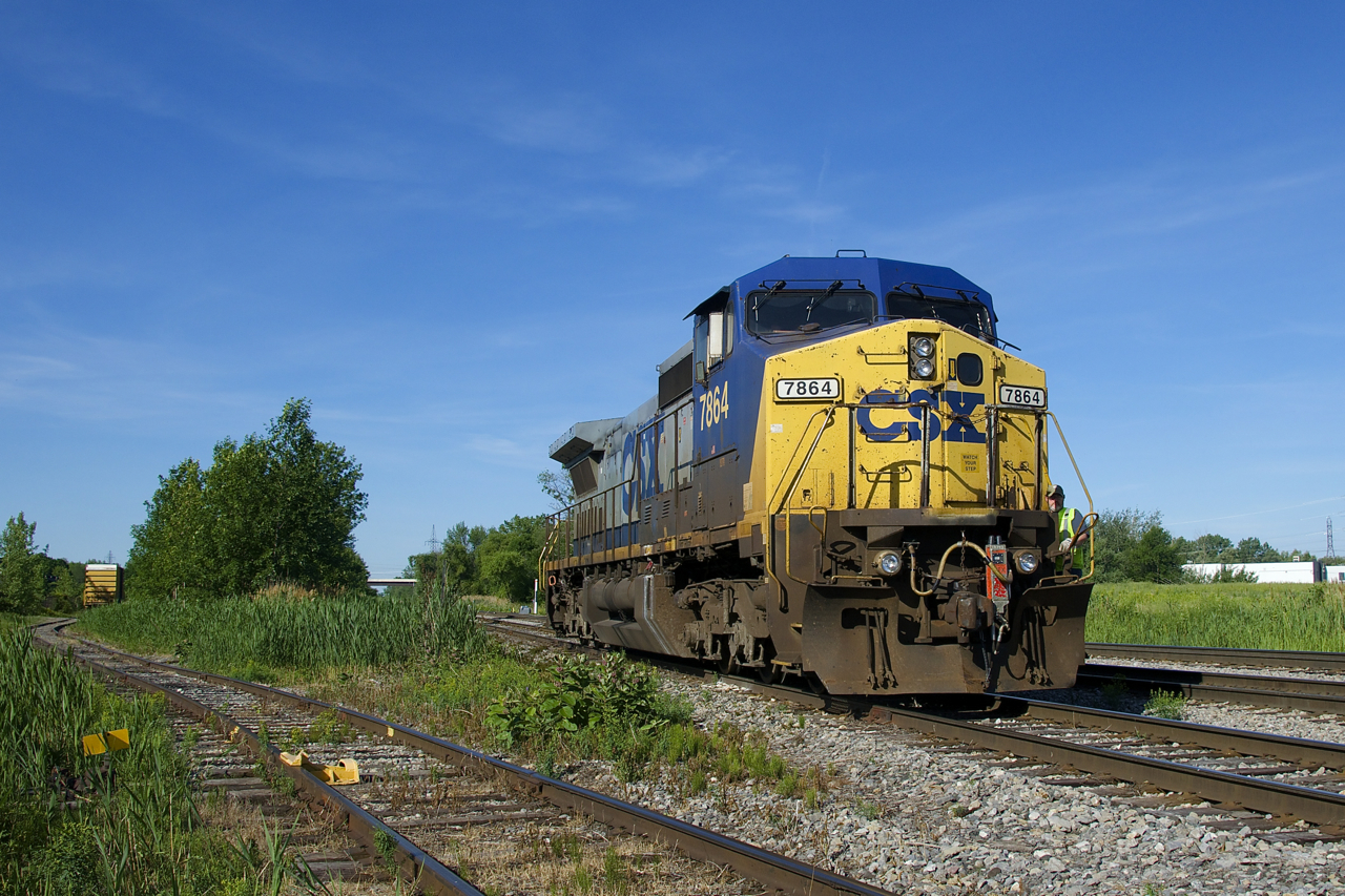 With an end-of-train device in the front coupler and the conductor riding the power, CSXT 7864 is heading to get its train ready before CSXT B763 heads south for Massena, with this single unit running long hood forward the whole way. At left a single boxcar is on the spur of an unknown client.
