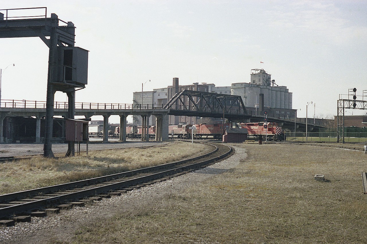 Here's a rather rough old image which I feel might appeal to those who knew and photographed at the Junction area of West Toronto in past years.
The whole of the long-gone old Weston Road bridge can be seen.
No traffic on it as it was closed a couple of years before this image was taken. Demolition was in 1983.
I had just gotten out of the car when a train rolled eastbound so grabbed this shot. Power is CP 5731, 4715, 4725, 5511 and 4709.  Best combination I would see this visit, and I almost missed it. Not much of a shot, but it is all now history.
That big grain facility that takes up so much land back there. Is that Campbell's Milling? I understand the structure was razed around 1992.  The area has all changed.