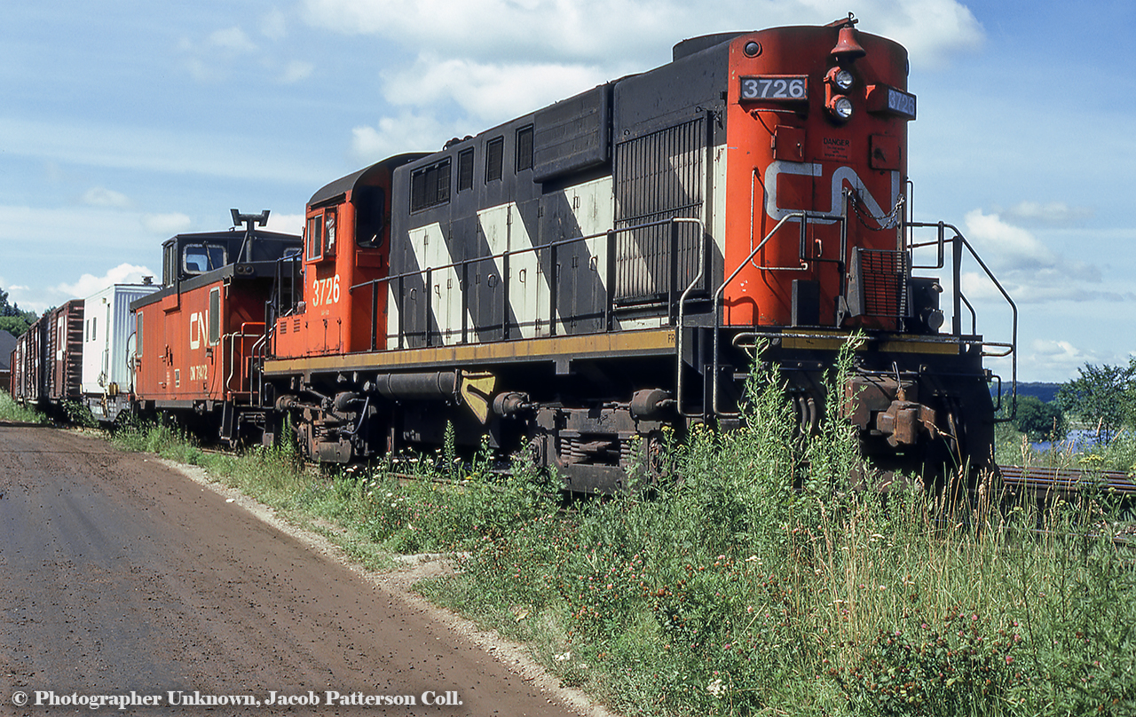 A sunny morning finds RS18 3726 and PSC van 79472 on the head end of a work train in the stub track near the Huntsville station. A sliver of which can be seen in the distance at left.Original Photographer Unknown, Jacob Patterson Collection Slide.
