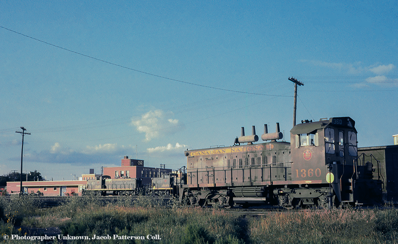 A summer evening finds a handful of green and gold GMD products in the yard at North Battleford, Saskatchewan near the CNR office.  The art deco lettering is still on the building on Railway Avenue as of 2019.  SW1200RS 1360 (GMD, 1960) would serve CN almost four decades, being retired in 1998 and sold to Canac.  Across the yard, A-1-A trucked GMD1s 1055 and 1033 can be seen.  Note the truck mounted sand boxes.  1055 (GMD, 1959) would be rebuilt to 1155 in 1991 and would be retired from CN in 1998, sold in 1999 to the Dardanelle & Russellville Railroad assigned to their Ouachita Railroad operation, followed by the Central Columbia & Pennsylvania, before returning to the Ouachita.  GMD1 1033 (built 1959) would be rebuilt into 1133 in 1983, and sold to the Cuban National Railway and if notes are correct, appears to have been renumbered 51208.  The rebuilding of both GMD1s into 1100 series units involved swapping the A-1-A trucks for flexicoil trucks from retired GP9s, larger fuel tanks, and other modifications.CN 1360 at Hamilton: September 1993.Original Photographer Unknown, Jacob Patterson Collection Slide.