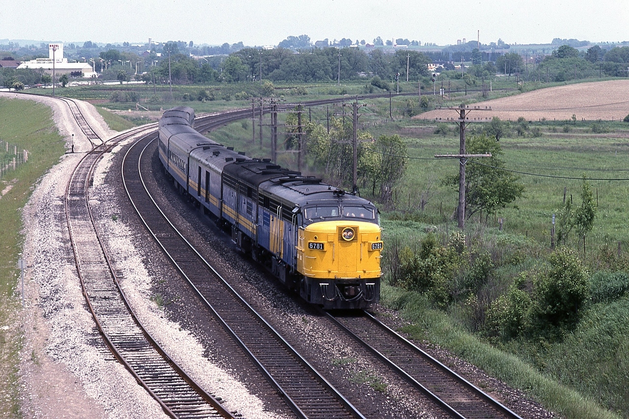 FPA-4 #6781 with a FPB-4 leads train #43 at mile 292 Kingston Subdivision


   The original Bowmanville Town spur crossed the 401 at grade – a level crossing -  on the far side of the trees above the train.   
 

   With completion of the Bowmanville 401 rail overpass ( circa 1983), the newly installed rail access to the Bowmanville Town spur, from the Kingston subdivision mile 291.4  is in place. The spur extended 1.4 miles north from the ( newly installed ) north service track .


   The spur was removed some time ago (mid 1990's ?) and the Bowmanville 401 rail overpass was removed overnight June 11, 2011.


   At Bowmanville, July 11 1983 Kodachrome by S.Danko


   More Bowmanville circa June 1982, look closely, the survey stakes are visible that mark the location of the planned new north service track.


       high speed curve  


   what's interesting:


   rsd-17 comment March 17, 2013: In my 16 years as a Bowmanvile resident the only time I saw a train on the spur, was a single GP-9 delivering the caboose that is now at Price’s Market (Hwy 2 & Lambs Road.) I didn’t get a shot as it was a dank rainy day and I was on my way to work. On a few occasions I walked through the Goodyear property saw evidence of activity (well cars and flat cars loaded with conveyer belt.) 


   notable:

there were three CNR level crossings east of Toronto on the  original  ‘ Dual Public Highway No. 401 ′ : 

( 1 ) the Pickering Town Spur, Kingston Sub mile 311.1 ( near the present Brock Road ), extended 0.7 miles north ; 

( 2 ) the Whitby Town Spur ( the original Whitby & Port Perry Railway ), mile 304.3 ( east of Brock Street ), extended 2.1 miles north;
 
( 3 ) the Bowmanville Town Spur, mile 290.6 extended 1.1 miles north ( as of 1973 ).

I recall passing over each of the crossings – many times – and as of 1973 all three crossings were in place (and the King’s Highway 401 speed limit was 70 m.p.h. before the Metric Imposition ). By 1979 given the 401 re-build and widening – only the Bowmanville level crossing remained. Interesting was that in town the Bowmanville spur crossed the front lawns (and driveways) of many houses on a street – I believe Hunt Street – north of Baseline Road. 


sdfourty