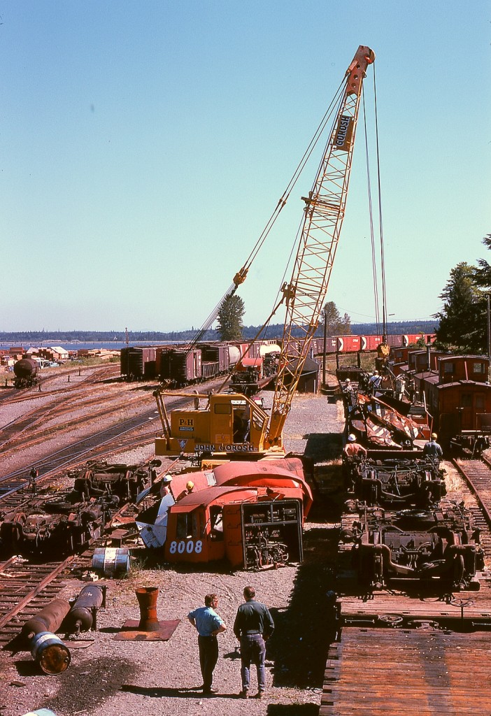 For me, the shot of E&N Baldwin scrapping at Wellcox in Nanaimo in July of 1974 that sums up the mess there is this, debris all about but operations continuing with cabooses all lined up and the yard office with scrap cars being scaled behind the crane’s boom.  In the foreground, the day and afternoon chargehands at Wellcox (a job I worked six years later) are observing.  That I was able to photograph it all from a variety of perches among the activity was due to the tolerance of Victoria locomotive foreman Hugh Albert Miller, who also organized and managed all the scrapping with no injury to any of us.  Thank you, Hughie.