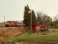 At Minnedosa, MB, where CP’s Minnedosa subdivision from the south joins to the Bredenbury sub. to the west, timetable train No. 977 with SD40-2 5756 and F7B 4439 and SD40 5514 is passing an early railway history display of caboose CP 431970 just before crossing the Little Saskatchewan River then Main Street.  Since then, CP FP7 4038 in maroon/grey with block lettering has joined the caboose in that display.