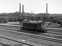 CN SW1200 7023 sits in the east end of Bathurst Street Yard in downtown Toronto, south of Front Street and east of Spadina Avenue, between switching duties in March of 1963. The team tracks and platforms in the background are full with 40' boxcars (the standard freight car of the day for freight, express and LCL shipments) unloading and loading cargo. One can spot a foreign Delaware, Lackawanna & Western (DL&W) "Route of the Phoebe Snow" car amid all the CN wafer-logo boxcars, and a new noodle-logo 40' repaint (it and the next car sporting yellow doors, initially meant to signify high-class merchandise service before being more commonly associated with CN boxcars in newsprint service).<br><br>According to timetables and track diagrams, this part of the yard was the K-200 series of team tracks, often noted as "Lower Yard" (see Robert Farkas' shot <a href=http://www.railpictures.ca/?attachment_id=35239><b>here</b></a>). Hendrie Cartage (a CN affiliated transportation company) operated out of this yard and handled freight and LCL shipments for CN and a variety of customers. Cargo such as food products, newsprint and papers, furniture, textiles (for Toronto's old downtown textile manufacturing industry) was often unloaded from 40' boxcars at the team tracks here, and transloaded onto trucks for local delivery in town, and vice-versa for outbound shipments.<br><br>Further east were the K-100 series of express and team tracks next to the CN Express building, that handled express shipments, customs and bonded cargo. Track K-101 was noted as the siding into the Express Building / Bond Shed. K-104 was the "Paper Platform" (outbound express newspaper shipments?), noted customers here include the Globe & Mail, Toronto Daily Star, Toronto Telegram, the Ryerson Press. Hendrie Cartage handled their own print and paper customers at Lower Yard's paper platform (Track K-201).<br><br>Auto and truck loads for Car-Go-Rail, auto brokers, select auto dealers, rental companies and manufacturers were noted as handled at the Auto Ramp tracks in the Parkdale area (see <a href=http://www.railpictures.ca/?attachment_id=45492><b>here</b></a>).<br><br>The <a href=http://www.railpictures.ca/?attachment_id=40508><b>CN Tower parking lot</b></a> displaced a lot of the K-100 & K-200 team tracks here in the mid-70's, and eventually succumbed to commercial redevelopment (the Metro Toronto Convention Centre, and Royal Bank data centre). The main Bathurst Street yard tracks (K-300 series) were reconfigured in the 1980's for GO Transit train storage, and today are know as GO's Bathurst North Yard. The old CN Express building west of Union Station was renovated into the Skywalk in the 1980's.<br><br>The track in the foreground lead up grade to CN's Simcoe Street yard and freight sheds at Front & Simcoe (south of the CP/Dominion Express freight sheds). Both CN and CP had freight sheds here, but CN's were demolished around 1967-68. CP's survived until the late 1970's before being demolished, but some facilities at King St. continued to exist for paper deliveries and team tracks into the 80's.<br><br>Background items of interest: CN's prominent Spadina Roundhouse with passenger power such as FPA4 and RS18's visible outside. Further in the background to the left was CP John Street Roundhouse and coach shop, with 40' ice reefers spotted nearby. TTR's Central Heating Plant is just visible off in the distance on the far left. The two smoke stacks in the middle of the photo (between the roundhouses) were for the City of Toronto's water filtration plant at Rees St. The silos on the waterfront at far right were for Maple Leaf Milling (demolished early 80's).<br><br>CN 7023: The CN 7000 series were made up of GMD SW9 and SW1200 units, 1200 horsepower "GS-12" switchers not equipped with roadswitcher features such as flexicoil trucks, larger fuel tanks, MU, and full end numberboards like the more common CN 1200- and 1300-series SW1200RS units were. Nevertheless, they along with the lower horsepower SW8 and SW900 units were common across the CN system at various terminals for local and yard switching duties well into the 1980's. Built in September 1956, 7023 later became 7723 (due to the 7000-series GP9RM rebuilds in the 80's that saw larger replacement local and switching power like the GP9's replace smaller, older, lower horsepower units like the SW8/900/9/1200 fleet) and eventually retired and disposed of.<br><br><i>Original photographer unknown, Dan Dell'Unto collection negative (large-format scanned with a DSLR, with some restoration work done).</i>