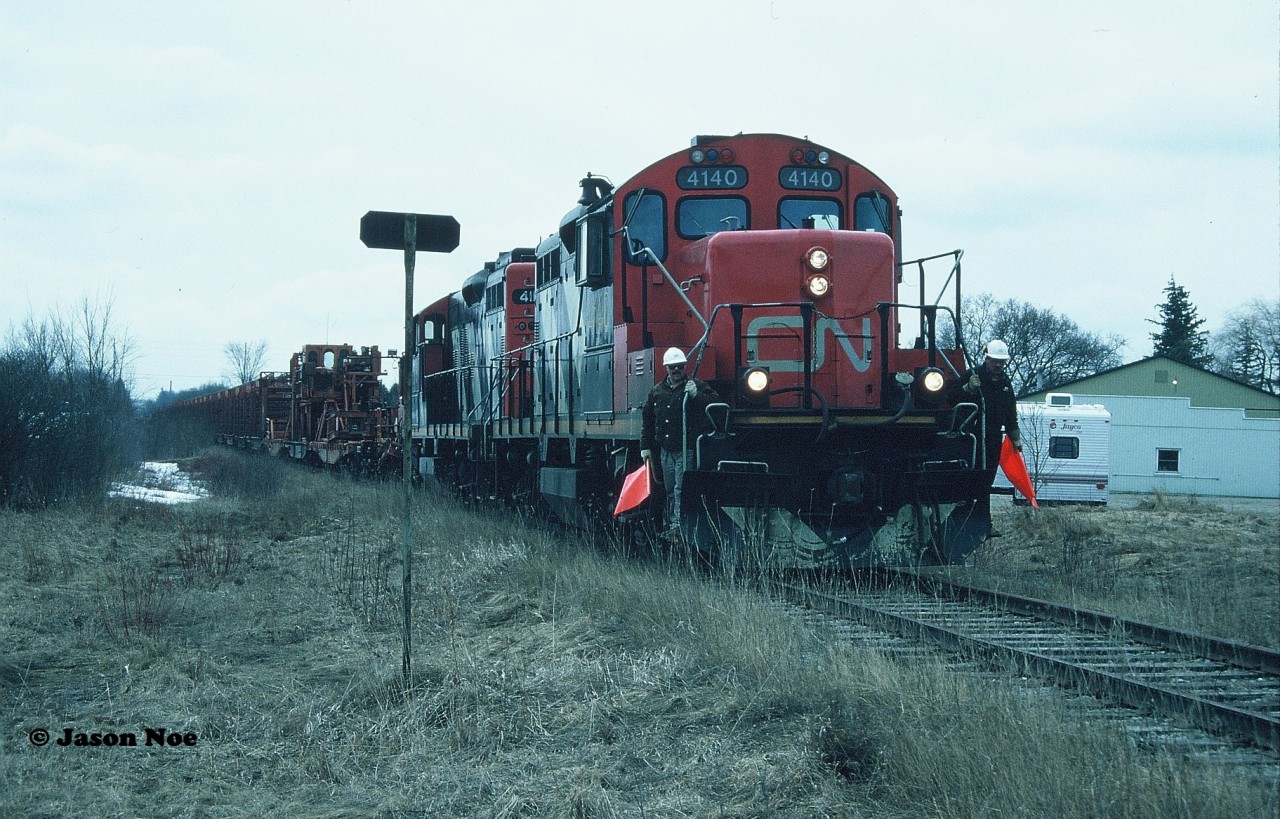 On April 4, 1995, the Canadian Transportation Agency had issued Order No. 1995-R-122, which officially gave CN permission to abandon all operations of the entirety of the Newton Subdivision from Stratford (mileage 1.17) to Palmerston at mileage 36.62. The order also included 1.41 miles of the mostly previously removed Kincardine Subdivision as well as a segment of the Owen Sound Subdivision from Palmerston (mileage 0.00) to Owen Sound (mileage 71.43) which encompassed a total distance of 108.29 miles. In short, CN was given permission to abandon and remove the last remaining pieces of the historic Bruce branchline’s from the once dominant railway city of Stratford, Ontario. 

This trackage lay in place for almost a full year until it was determined by CN that the heavy rails between Harriston and Listowel were required on other parts of their system vs. being scrapped. So in turn at end of March 1996 a lengthy empty rail train had reportedly arrived in the Stratford yard. 
With all signs pointed to the rail train being destined for Palmerston on the following Monday I had basically begged my dad to call in sick for me to school so I would be able to photograph it. At that time there was no internet, no cell phones or texting so all breaking railway news was basically conveyed through phone calls or updates from the train crews themselves. As much as I wanted to tell my dad that this was a sure thing so he could make the call, there was a chance it wasn’t even going to happen that day. Thankfully, early that morning he made the decision to call my high school and mark me down as sick. With the final approval, a friend and I then drove to Stratford where all the unknowns would be answered. Not long after arrival, CN GP9RM’s 4140 and 4115 departed the yard at Newton Junction hauling the complete rail train eventually destined for Palmerston. 

Under an overcast sky as the last remnants of winter gave way to spring, two foremen protecting are seen prepared to protect the aging crossing with CN 4140 and 4115 slowly approaching Perth County Road 119, just north of Straford on the Newton Subdivision. From here, the same road had paralleled the line for several miles north towards the small towns which CN had served for decades with the rusty rails traversing through Ontario’s farmland to legendary Palmerston. 
A solid thank you dad as the chase would begin.