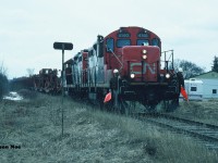 On April 4, 1995, the Canadian Transportation Agency had issued Order No. 1995-R-122, which officially gave CN permission to abandon all operations of the entirety of the Newton Subdivision from Stratford (mileage 1.17) to Palmerston at mileage 36.62. The order also included 1.41 miles of the mostly previously removed Kincardine Subdivision as well as a segment of the Owen Sound Subdivision from Palmerston (mileage 0.00) to Owen Sound (mileage 71.43) which encompassed a total distance of 108.29 miles. In short, CN was given permission to abandon and remove the last remaining pieces of the historic Bruce branchline’s from the once dominant railway city of Stratford, Ontario. 
<br>
This trackage lay in place for almost a full year until it was determined by CN that the heavy rails between Harriston and Listowel were required on other parts of their system vs. being scrapped. So in turn at end of March 1996 a lengthy empty rail train had reportedly arrived in the Stratford yard. 
With all signs pointed to the rail train being destined for Palmerston on the following Monday I had basically begged my dad to call in sick for me to school so I would be able to photograph it. At that time there was no internet, no cell phones or texting so all breaking railway news was basically conveyed through phone calls or updates from the train crews themselves. As much as I wanted to tell my dad that this was a sure thing so he could make the call, there was a chance it wasn’t even going to happen that day. Thankfully, early that morning he made the decision to call my high school and mark me down as sick. With the final approval, a friend and I then drove to Stratford where all the unknowns would be answered. Not long after arrival, CN GP9RM’s 4140 and 4115 departed the yard at Newton Junction hauling the complete rail train eventually destined for Palmerston. 
<br>
Under an overcast sky as the last remnants of winter gave way to spring, two foremen protecting are seen prepared to protect the aging crossing with CN 4140 and 4115 slowly approaching Perth County Road 119, just north of Straford on the Newton Subdivision. From here, the same road had paralleled the line for several miles north towards the small towns which CN had served for decades with the rusty rails traversing through Ontario’s farmland to legendary Palmerston. 
A solid thank you dad as the chase would begin. 
