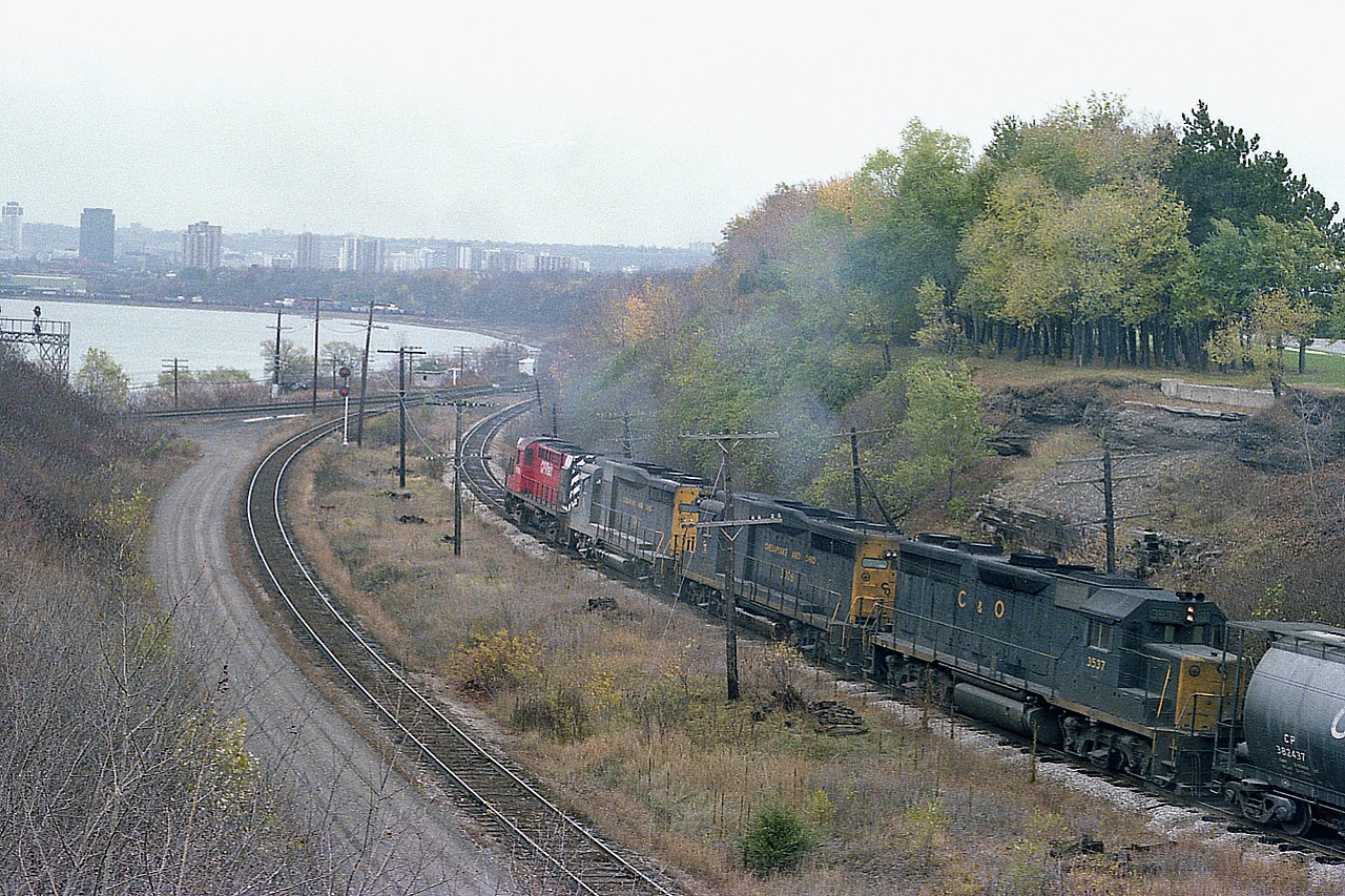 For me, this image is powerfully nostalgic.  For it is a CP detour train, running down from the GALT sub into Hamilton and back out to Toronto via the CN on account of the big Nov 1979 train derailment in Mississauga. Over 200,000 people were evacuated as tank cars threatened to blow; and it would be the single most intense derailment in Canada's history in terms of mass evacuation.
Anyway, after this train wound its way down the hill from Waterdown, I ran across the roadway and grabbed this image as it rolled up to the area known on CN as Hamilton Jct. The power on this train was impressive.
CP 8679 leading followed by C&O 3046, 3006 and 3532. Loved seeing GP30s.
Added note: A few years previous, I think 1975; there was a wooden bridge over to York which crossed the tracks, from Valley Inn Rd. It had a rather severe load limit.  A "not too bright" truck driver ignored the sign, and as a result the bridge collapsed.  You can see the concrete remains on the right hillside. And straight ahead of CP 8769 in the distance the CN section shack and 'Hamilton Jct' sign can be seen.
The CN "Cowpath" is on the left, which is the link to the Dundas sub and West from Hamilton.