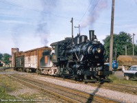 A typical summer evening in a small, Southern Ontario town finds the local yard switcher wobbling up the yard lead across Downie Street while townsfolk pause their business to wait for the hissing beast to pass.  The engineer aboard Canadian National O-12-a, 0-6-0 switcher 7411 looks intently towards the rear of his train watching for hand signals from the brakemen as they shove around the bend into Stratford yard.  The battlemented tower of Stratford's station and smoke from another locomotive loom in the background, and like the steam power seen around the yard and still emerging from the big shop, the tower is on borrowed time.  It will be demolished during the 1960s.  Originally part of the Canadian Northern Railway fleet built by CLC of Kingston, the 1920-built switcher would survive until scrapping in August, 1958.<br><br>A <a href=http://www.railpictures.ca/?attachment_id=45815>recent post by Steve Host,</a> snapped in 2020, shows a similar scene as shot from a couple hundred feet further down the road.<br><br><i>Original Photographer Unknown, Al Chione Duplicate, Jacob Patterson Collection Slide.</i>