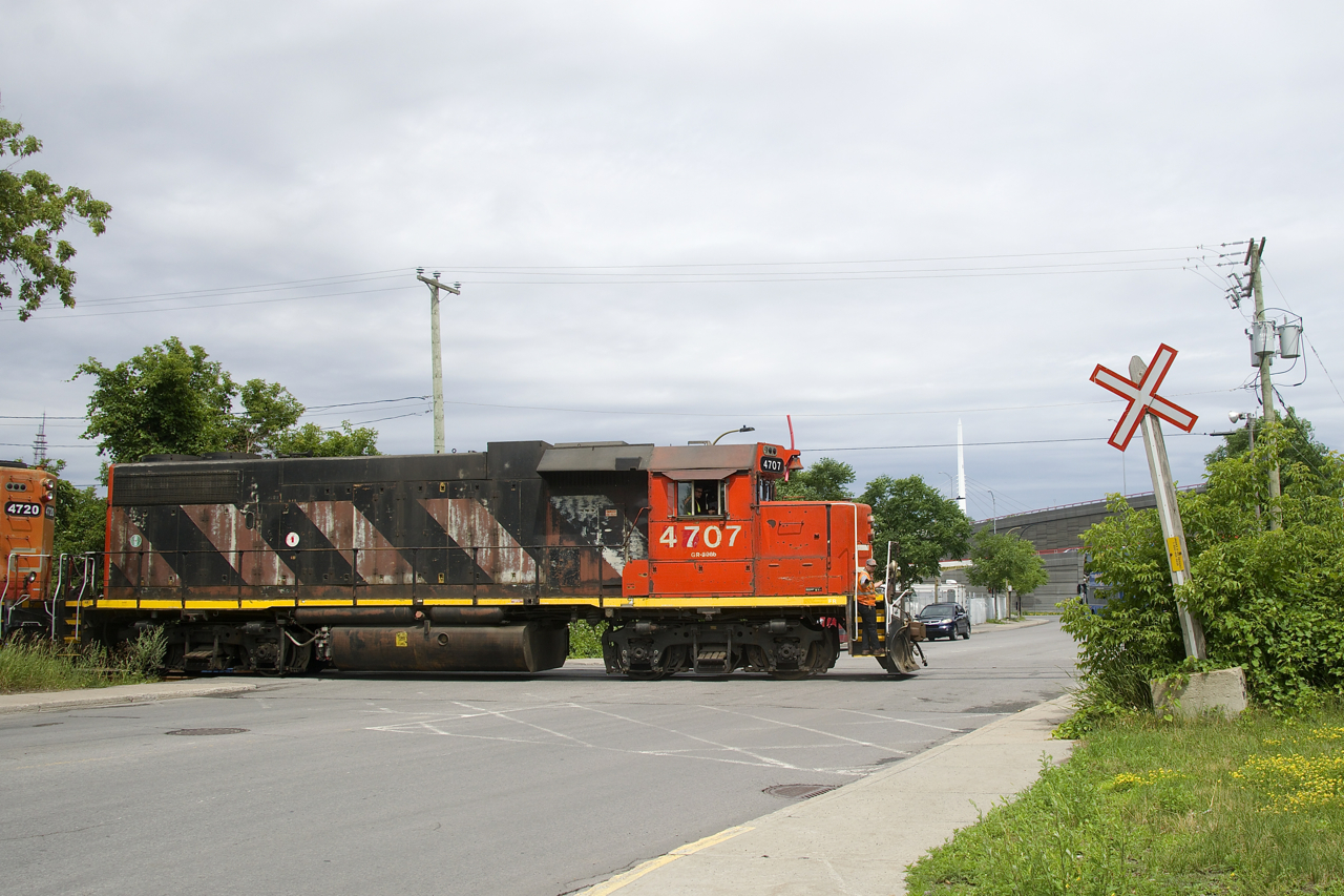 The conductor waves after flagging the busy Monk Boulevard crossing as the Pointe St-Charles Switcher departs the Turcot Holding Spur with two cars, after having dropped off one.