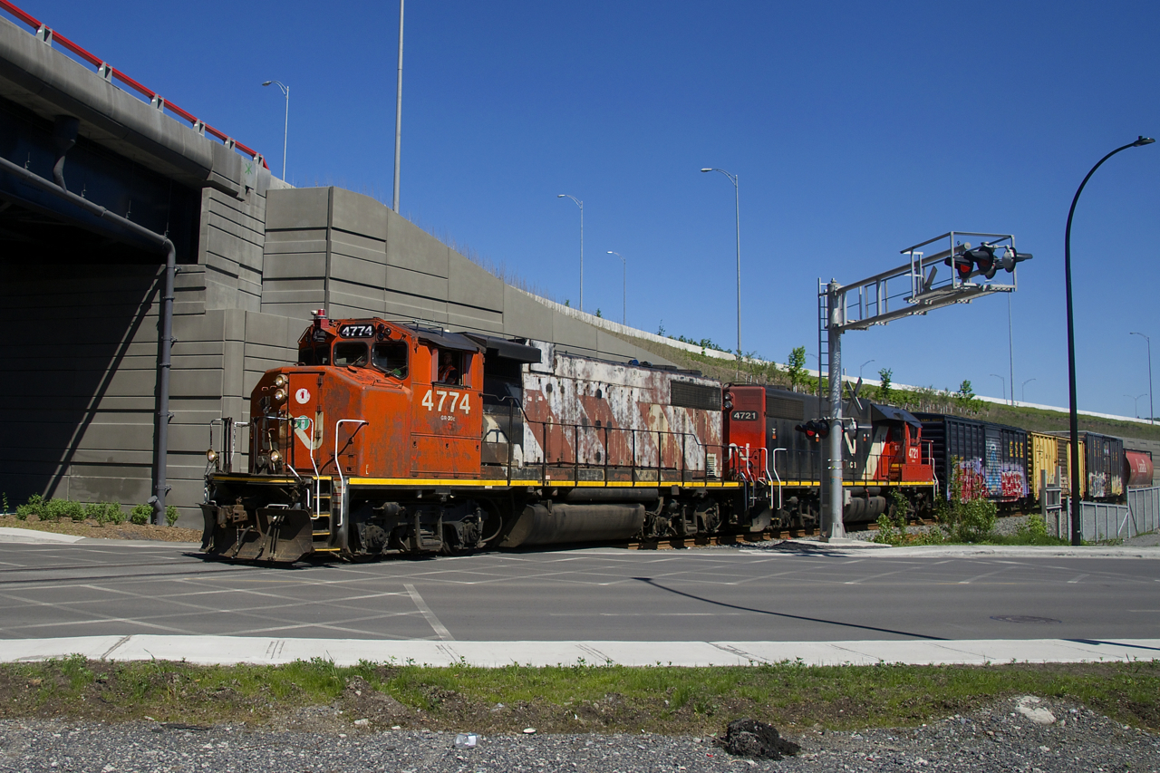 The Pointe St-Charles Switcher is crossing Notre-Dame Street, on its way to bring cars to the Kruger plant. The train is about to go under the rebuilt Turcot interchange.