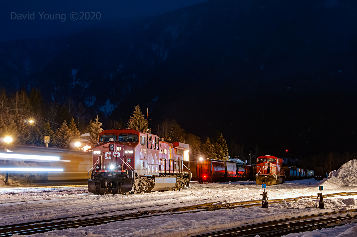 A dark, winter's night in downtown Revelstoke is broken by the reverberation of a westbound accelerating out of town after a crew change. In the yard a set of GE locomotives idle away, sharing company with an eastbound grain empty parked in the yard.