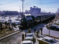 Returning from a run to the Elmira Maple Syrup Festival, Ontario Rail Association's ex CPR D10h number 1057 is seen southbound (timetable eastbound) crossing Woolwich Street and Speedvale Avenue in Guelph.  Just a few years prior to this, Speedvale Avenue marked the northernmost city limit of Guelph, and the Co-op seen in the background would be "out in the country."  Note the "City Limit" sign in <a href=https://s3.amazonaws.com/pastperfectonline/images/museum_51/193/2009324070.jpg>this 1954 view.</a><br><br>The short stub siding at right on the east side of the Goderich subdivision mainline served the privately owned freight shed at far right (seen <a href=https://s3.amazonaws.com/pastperfectonline/images/museum_51/193/2009324018.jpg>here at centre</a> in 1976).  The shed served a number of small cartage firms and rail service was seen sporadically over the years.  Behind the train, the rooftop sign of the local Esso station is seen, which today remains an empty lot.  Across Woolwich Street, <a href=https://s3.amazonaws.com/pastperfectonline/images/museum_51/198/2013391246.jpg>Root Home Centre</a> (part of Home Hardware Stores) can be seen.  Now home to the Rexall Pharmacy, the site originally housed a <a href=https://s3.amazonaws.com/pastperfectonline/images/museum_51/116/2012383.jpg>Loblaws Supermarket.</a><br><br>Looming over the whole scene (including the smokestack at left) is the sprawling United Dairy Producer's Co-operative (officially Gay Lea by this time).  Originally constructed in 1949 (silos circa 1960), the Co-op was built on farmland owned by Guelph-born Operatic tenor, and later manager of the Metropolitan Opera of New York City, <a href=https://archive.macleans.ca/article/1939/6/15/edward-johnson-of-guelph>Edward Johnson (1878 - 1959),</a> with the land having been sold in 1947 to the United Co-operative of Ontario.  The Co-op would be renamed United Dairy and Poultry Co-operative in 1958, and later the United Dairy Producer's Co-operative in 1967.  In 1972, the organization was renamed Gay Lea Foods, which still operates the site today as one of only 5 facilities in Ontario owned by the co-operative of over 1,200 dairy farmers* (*per 2010 Guelph Mercury article).  The towering feed mill silos would be demolished in the 1990s and a processing plant built in it's place.<br><br>Note the "Danger Bell" sign used at Speedvale Avenue <a href=https://s3.amazonaws.com/pastperfectonline/images/museum_51/193/2009324067.jpg>in this 1954 image.</a>  The box above the crossbuck would illuminate the word "DANGER" with approaching trains.  Another was located at the Concession 11 crossing just south of Corwhin, known by crews as "Danger Bell".<br><br>A boxcar is seen <a href=https://s3.amazonaws.com/pastperfectonline/images/museum_51/193/2009324065.jpg>on the stub siding in 1954.</a>  Note the sign at centre which would be the northern mileboard for Guelph.<br><br><i>Bruce Lowe Photo, Eric Repaci Collection Slide.</a>