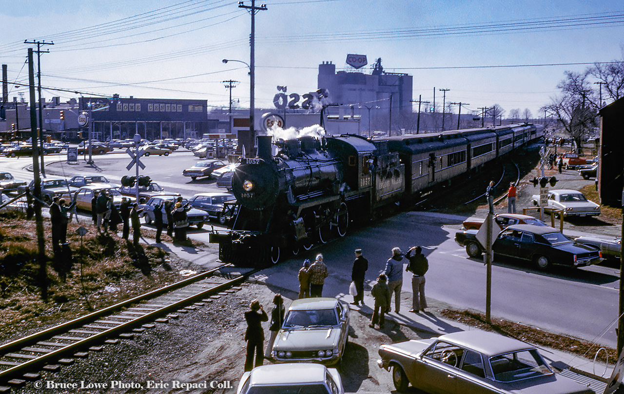 Returning from a run to the Elmira Maple Syrup Festival, Ontario Rail Association's ex CPR D10h number 1057 is seen southbound (timetable eastbound) crossing Woolwich Street and Speedvale Avenue in Guelph.  Just a few years prior to this, Speedvale Avenue marked the northernmost city limit of Guelph, and the Co-op seen in the background would be "out in the country."  Note the "City Limit" sign in this 1954 view.The short stub siding at right on the east side of the Goderich subdivision mainline served the privately owned freight shed at far right (seen here at centre in 1976).  The shed served a number of small cartage firms and rail service was seen sporadically over the years.  Behind the train, the rooftop sign of the local Esso station is seen, which today remains an empty lot.  Across Woolwich Street, Root Home Centre (part of Home Hardware Stores) can be seen.  Now home to the Rexall Pharmacy, the site originally housed a Loblaws Supermarket.Looming over the whole scene (including the smokestack at left) is the sprawling United Dairy Producer's Co-operative (officially Gay Lea by this time).  Originally constructed in 1949 (silos circa 1960), the Co-op was built on farmland owned by Guelph-born Operatic tenor, and later manager of the Metropolitan Opera of New York City, Edward Johnson (1878 - 1959), with the land having been sold in 1947 to the United Co-operative of Ontario.  The Co-op would be renamed United Dairy and Poultry Co-operative in 1958, and later the United Dairy Producer's Co-operative in 1967.  In 1972, the organization was renamed Gay Lea Foods, which still operates the site today as one of only 5 facilities in Ontario owned by the co-operative of over 1,200 dairy farmers* (*per 2010 Guelph Mercury article).  The towering feed mill silos would be demolished in the 1990s and a processing plant built in it's place.Note the "Danger Bell" sign used at Speedvale Avenue in this 1954 image.  The box above the crossbuck would illuminate the word "DANGER" with approaching trains.  Another was located at the Concession 11 crossing just south of Corwhin, known by crews as "Danger Bell".A boxcar is seen on the stub siding in 1954.  Note the sign at centre which would be the northern mileboard for Guelph.Bruce Lowe Photo, Eric Repaci Collection Slide.