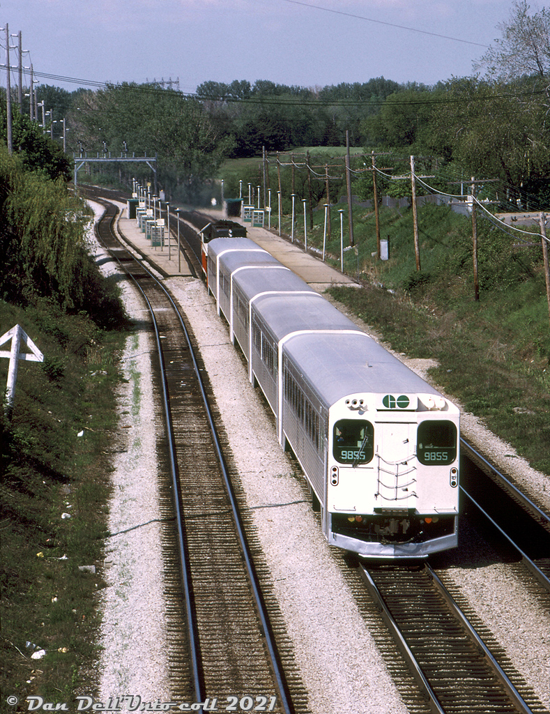 GO Transit cab car 9855 leads a train of five single-level Hawker Siddeley commuter cars eastbound on CN's Oakville Sub towards Brown's Line overpass in southwest Etobicoke, after making its stop at Long Branch GO station. The sun angle suggests this is a late morning train, and timetables indicate GO operated an hourly afternoon service on the Lakeshore Line. A "Railway Junction, One Mile" triangular sign juts out on the left for eastbound trains approaching Canpa Junction.

In preparation for the launch of GO Transit's commuter rail service in 1967, it was decided the three old CN station stops serving Long Branch, Dixie Road, and Lakeview were to be consolidated into a new Long Branch GO station at Mile 9.6 of CN's Oakville Sub, located more to the west of the former location (Mile 8.8, by 30th Street) to better connect with the nearby TTC Long Branch streetcar loop. By that time, it doesn't appear there were any station buildings at those old scheduled CN stops, aside from a shelter at Dixie.

Photographer unknown, Dan Dell'Unto collection slide.