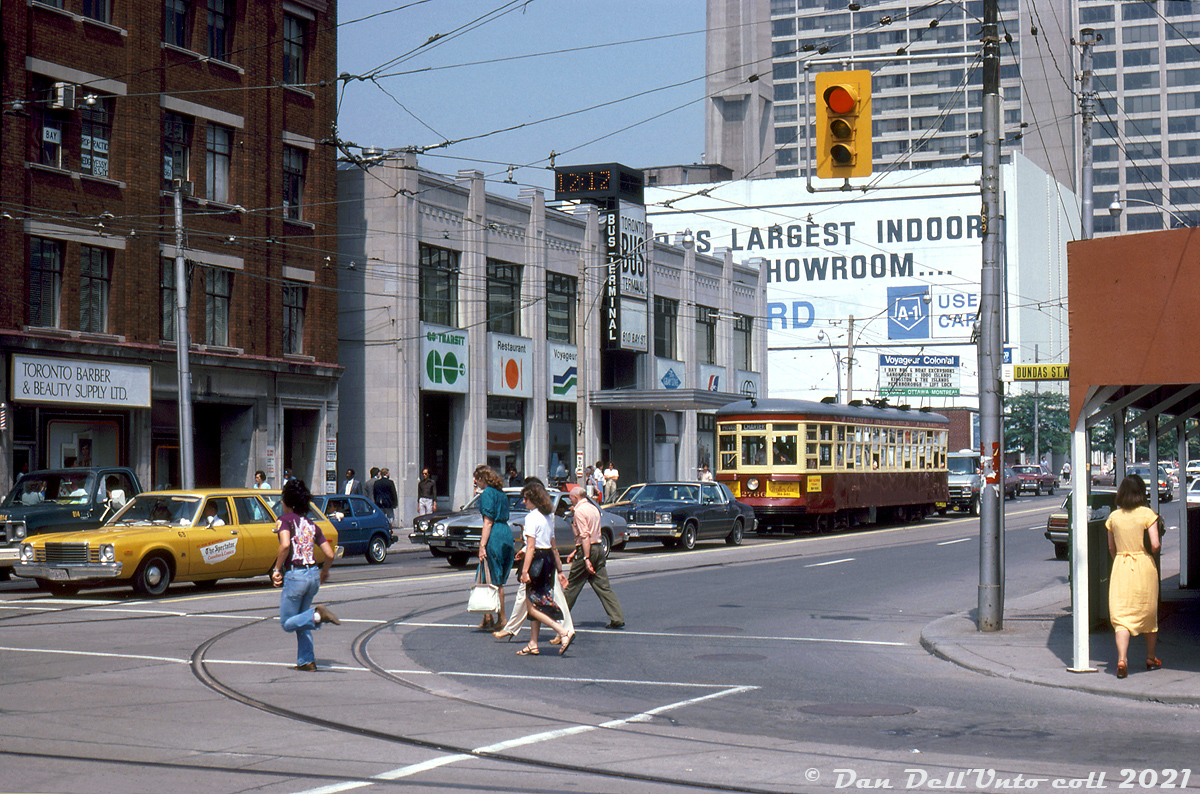 A sunny summer afternoon around 12:12pm (according to the terminal clock) finds TTC Peter Witt streetcar 2766 operating on a fantrip charter, waiting in traffic southbound on Bay Street at Dundas as pedestrians cross in the foreground (in front of a station wagon marked for "The Spectator" (Hamilton Spectator?)). The old Peter Witt is one of a handful retained, re-acquired or borrowed by the TTC for a downtown Tour Tram service that ran for a few years in the 1970's, after the last of the Witts had been retired in 1965. They were popular for transit enthusiast charters and fantrips during their reprieve, and the TTC still retains car 2766 today for rare trips out around town.

In the background is the the Toronto Coach Terminal, downtown Toronto's main intercity coach terminal located at the southwest corner of Bay and Edward. Operators running out of the terminal are displayed on the signage outside: GO Transit (note slightly different logo with stylish arrow), Voyageur Colonial (east coast coach operator later absorbed by Greyhound, note billboard in the background), Gray Line tours, Greyhound Canada, and Gray Coach Lines. It initially opened December 19th 1931 and served as the main Toronto hub for the TTC's interurban coach operator Gray Coach Lines (sold off to Greyhound in the 90's). As the years went by, the terminal proved to be a poor location due to its distance from major highways (QEW/Gardiner/Hwy 427/Hwy 401) and the need for buses to navigate busy downtown traffic.

GO Transit began its own bus operations here in 1970, but in the 90's moved to loading right outside of Union Station on Front Street, until a new bus terminal opened in 2001 (the site of the old CP Express Building). GO recently moved into yet another new bus terminal south of the rail corridor in December 2021, its bus services out of Union outgrowing the previous one!

For the longest time, Greyhound Canada had been the main tenant of the Toronto Coach Terminal. But that all changed when they suspended all Canadian operations due to the COVID pandemic in May 2020, and announced a year later in May 2021 that they would be ceasing all of their Canadian operations permanently. Ontario Northland's bus service was the final operator to use the terminal, but it wasn't long before they moved to the new GO bus terminal downtown, and the old Toronto Coach Terminal on Bay would close on July 4rd 2021. The main building and lobby area (that had underwent restoration) is on the city's heritage register, so it is expected it would be retained and incorporated in whatever redevelopment plans will follow.

Photographer unknown, Dan Dell'Unto collection slide.