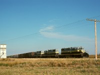 Under a glorious Peace River country clear sky on Friday 1976-09-24, Northern Alberta Railways’ GSL Turn is returning from the CN Great Slave Lake line connection at Roma Jct. to McLennan with its usual trio of SD38-2s, this day 402 plus 404 plus 401, passing the lone grain elevator at Judah at mileage 41.6 after the 8-mile climb from Peace River, where each unit was rated to handle 1200 tons.  In another 43 miles they will be at their home terminal.