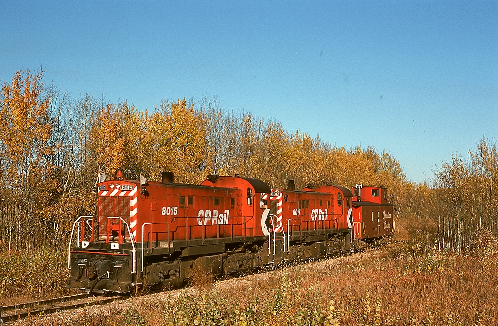 A maze of branch lines operated out of Prince Albert, with CP often utilizing CN lines to access CP branches.  One was the Nipawin Turn for 18 miles on the CN Paddockwood sub. to a junction at Sharpe with the CP White Fox sub. eastward to Nipawin.  Typical service was a pair of MLW RS-23s and a caboose on CN from Prince Albert to Sharpe then on CP to Meath Park, then picking up grain loads through to Nipawin, then empties westward with setoffs at active grain elevators up to Meath Park, then running cab hop home to Prince Albert.  On Tuesday 1976-09-28, that is what 8015 and 8017 are doing, westbound at Gobeil Road and less than a mile from CN track at Sharpe.

Today, this is empty grade; track extends northward from Prince Albert only 8 miles to White Star (Carleton Trail) and westward from Nipawin to Choiceland (Torch River Rail).