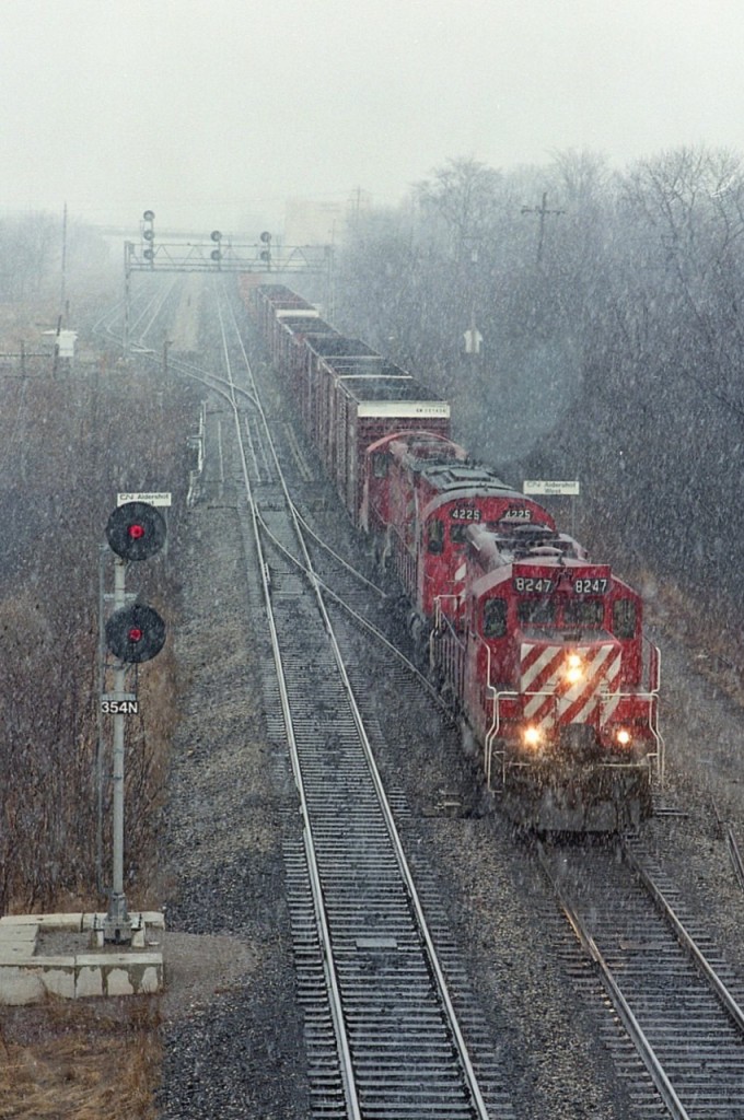 Some days got so miserable I wondered what the heck I was doing out. After all, the nearest "action" is best around Aldershot, away from my home by about 25 miles. But, it was my day off work.
So this day, not only is it cold and wet, the sleet started. Gawd. Might as well try something different, as the train was moving very slowly and just getting to accelerating for Hamilton as seen from my position on the Lemonville Rd overpass. For you film guys, I set the camera at 60th and f8,(400 ISO medium format) balancing it on the bridge railing.
Streaks of sleet. Not as good as I had hoped, but the fact CP no longer runs over the Oakville plus all this power is now gone from the CP roster at least makes this interesting. Power is CP 8247, 4225 and 4241.