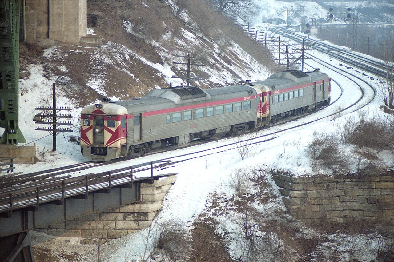 The morning CP Dayliners, Budds 9112-9020 roll toward Hamilton from Toronto; en route to Buffalo on a rather nice softly lit early morning.  The view is from underneath the McQuesten High Level bridge which connects Hamilton with Aldershot. Passenger service from Toronto to Buffalo and return daily was bound by agreement over CP/TH&B until April 25, 1981; when this train ceased to exist. For most of us at the time, it was just another passenger train to view as it passed @0930 while waiting for interesting freights. :o)
In the photo, the double track line to Niagara is on the right, and in the background Hamilton Jct where CP and CN lines split. Configuration has all changed in the past few years as the area has been beefed up for the future GO service to Niagara Falls; which, we are told, will happen some day.