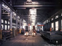 When one thinks of John Street they think of CP's famed roundhouse, that maintained CP's fleet of steam and diesel passenger power, RDC's and in later years vintage Alco/MLW switchers until it closed in the mid-80's. But there were also other facilities on site at John Street: here's a rare look inside CP's 3-track John Street car shops building, located near the roundhouse just south of the CN tower, and used to maintain CP's fleet of passenger cars operating on trains out of downtown Toronto since it was constructed in the late 1920's for steam-era operations.<br><br>Three stainless steel Budd-built passenger cars used on The Canadian are in for work, including a "Park" series observation-dome-lounge car (likely Sibley Park). By this time in the mid-70's, service cuts and rationalization of CP's passenger network left few passenger trains to maintain out of Toronto. Trains #11/#12, the Toronto-Sudbury sections of "The Canadian" still called John Street home, along with the Peterborough and Buffalo Budd RDC runs. CP also operated piggyback ramps out of its John Street yards downtown starting in the 50's, and the carshops were also utilized to service CP's fleet of 50xxxx-series piggyback flatcars, like the one on the right and another barely visible on the left.<br><br>Down the middle between two tracks, passenger car wheelsets equipped with Budd's disc brakes and patented "Rolokron" anti-slip skid system are lined up in the rail indents between tracks below the 15-ton Northern overhead crane, ready for any change-outs. Truck springs of various sizes line the floor nearby, and a pile of brakeshoes can be seen further down.<br><br>From what I gather, what little passenger car servicing that remained here after VIA took over in 1978 was moved to VIA's ex-CN Spadina Coachyard at some point in the early-mid 80's (stainless steel ex-CP cars started appearing there before VIA's move to the TMC), and the car shops continued to be in use servicing freight equipment like piggyback and container flatcars (most piggyback operations had been moved to Obico, but nearby Parkdale Yard had been converted into a container handling facility) and storing work cars until John Street was shut down in July of 1986. The roundhouse was donated to the city by CP, but the car shops building was eventually demolished in the following years.<br><br><i>Bernie Smith photo, Dan Dell'Unto collection slide (from what I gather, that's Bernie's son in the photo, who made a few appearances in his photos).</i>