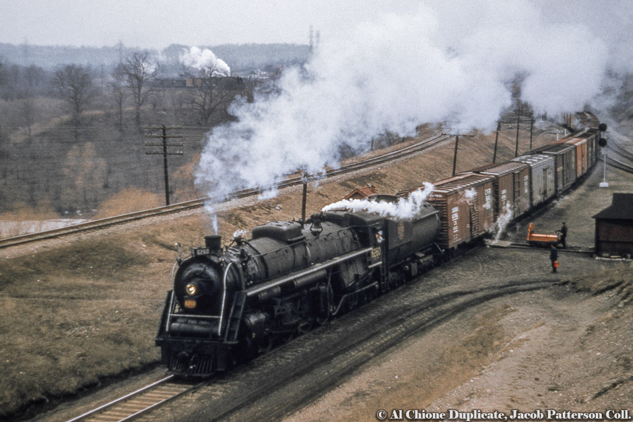 A section crew sits clear of the main for CNR U-2-h 6260 (MLW, January 1944, scrapped July 1961) and it's freight coming down the hill from Dundas and onto the cowpath.  Almost entirely boxcars visible, save for one silver, 8-hatch ice reefer third up.Note the CPR freight descending the Goderich Sub at left... top of the frame just beside the plume of steam.More CNR U-2-h, by Bill Thomson:Scarborough, 1955.Mimico, 1956 (1).Mimico, 1956 (2).Original Photographer Unknown, Al Chione Duplicate, Jacob Patterson Collection
