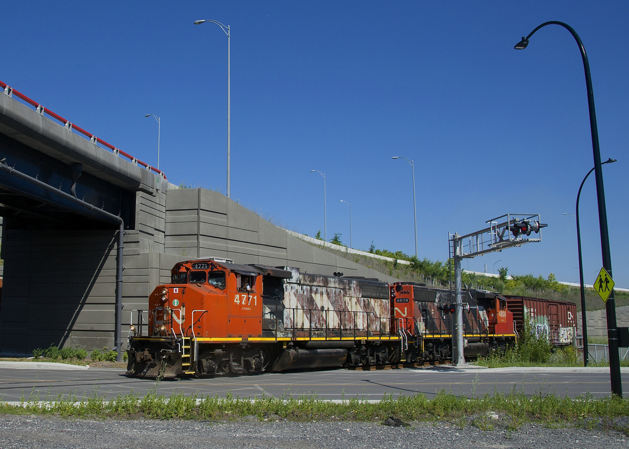 The Pointe St-Charles Switcher has a single boxcar for Kruger as it crosses Notre-Dame Street with CN 4771 & CN 4808 for power as the conductor gives a wave.